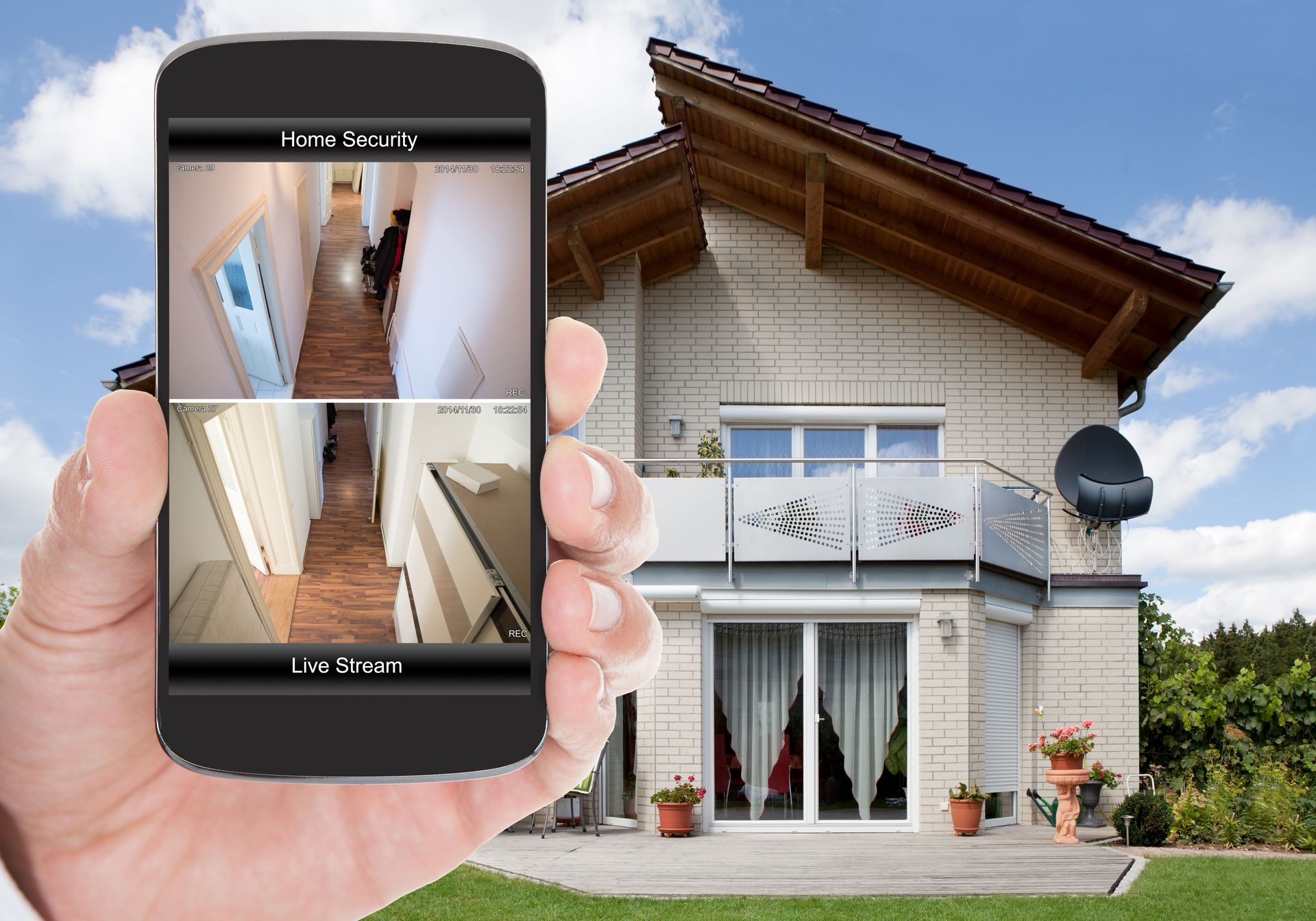 Hand holding phone displaying home security camera footage, with house in background.