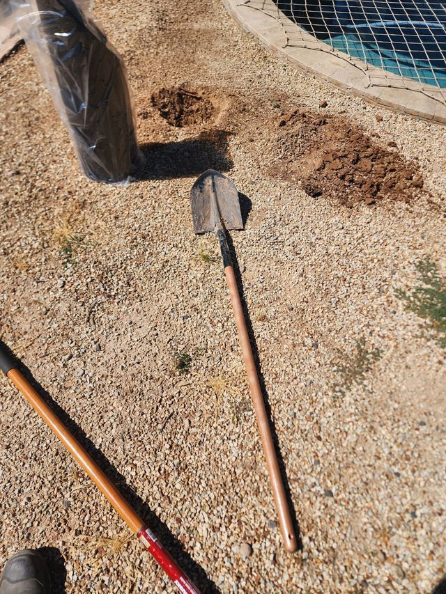 Shovel on gravel ground next to holes, a bag, and a pool.