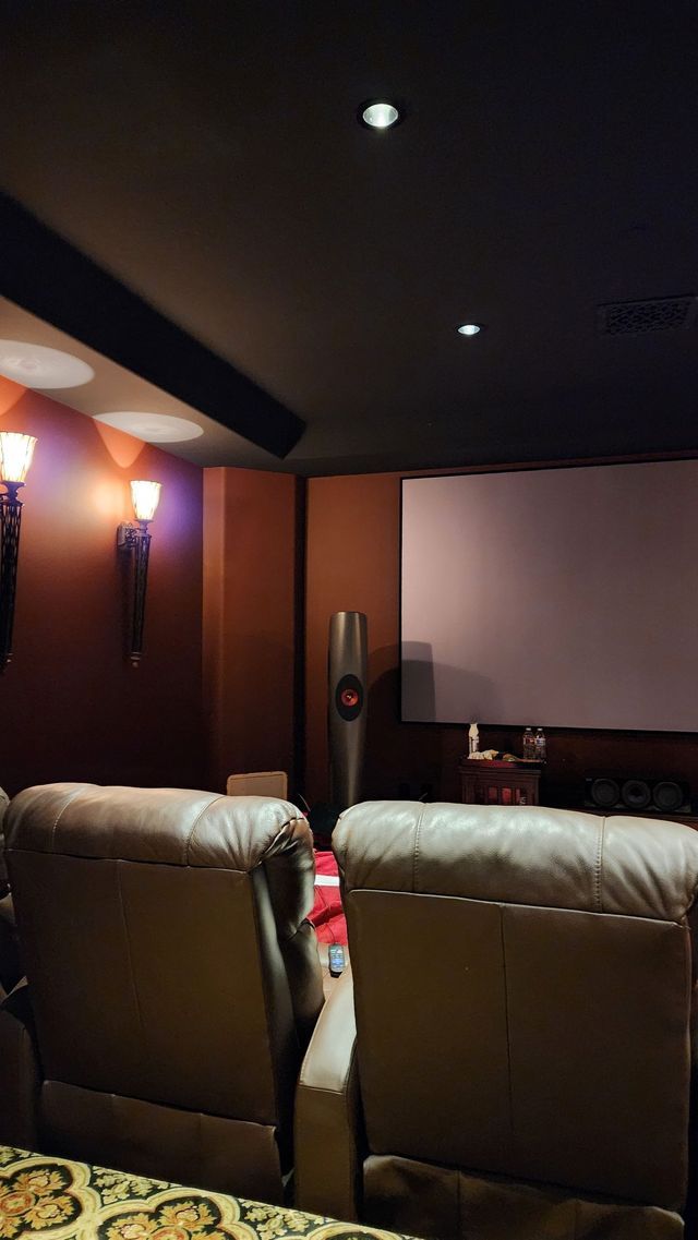 Home theater with tan leather recliners, screen, and brown walls, illuminated by dim lighting.