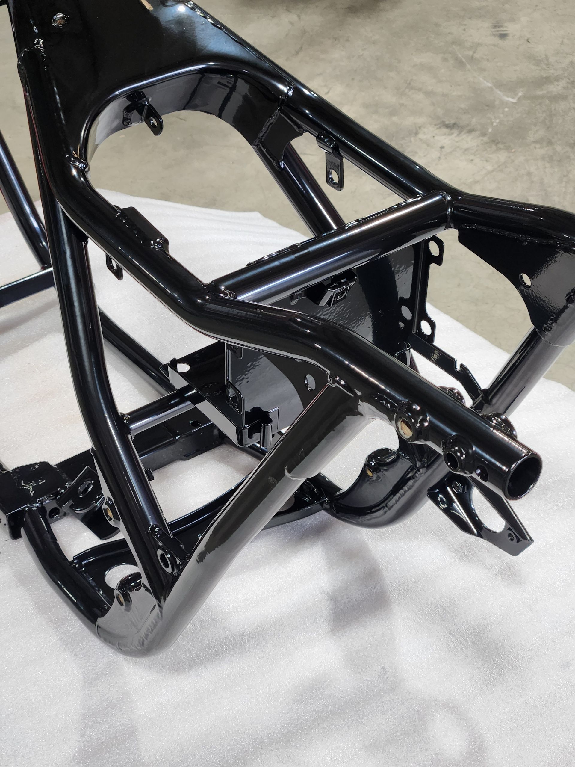 Black motorcycle frame/chassis on a workshop floor, painted glossy black with exposed metal components.