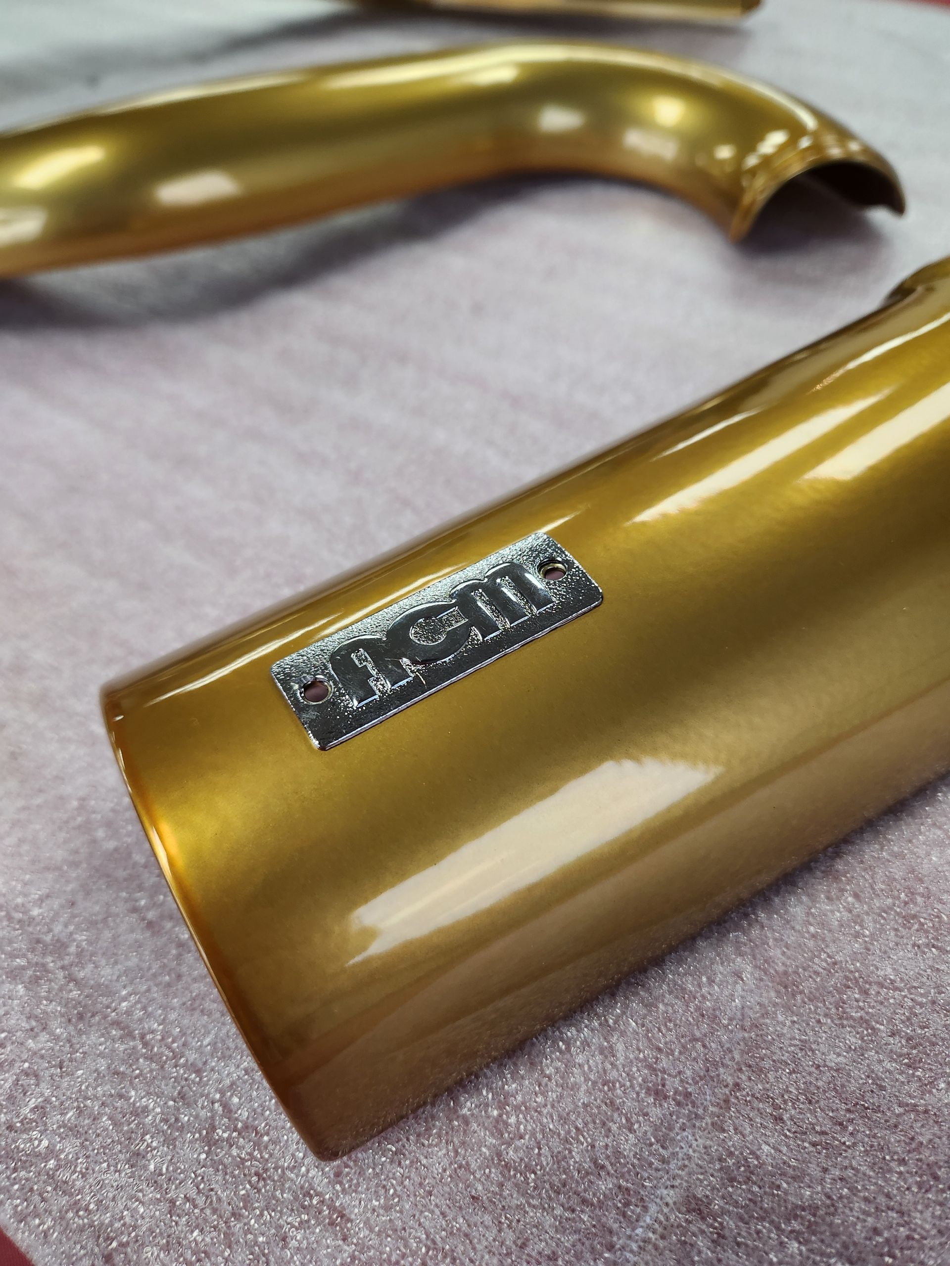 Gold-colored custom metal part with a small rectangular emblem on a fabric surface