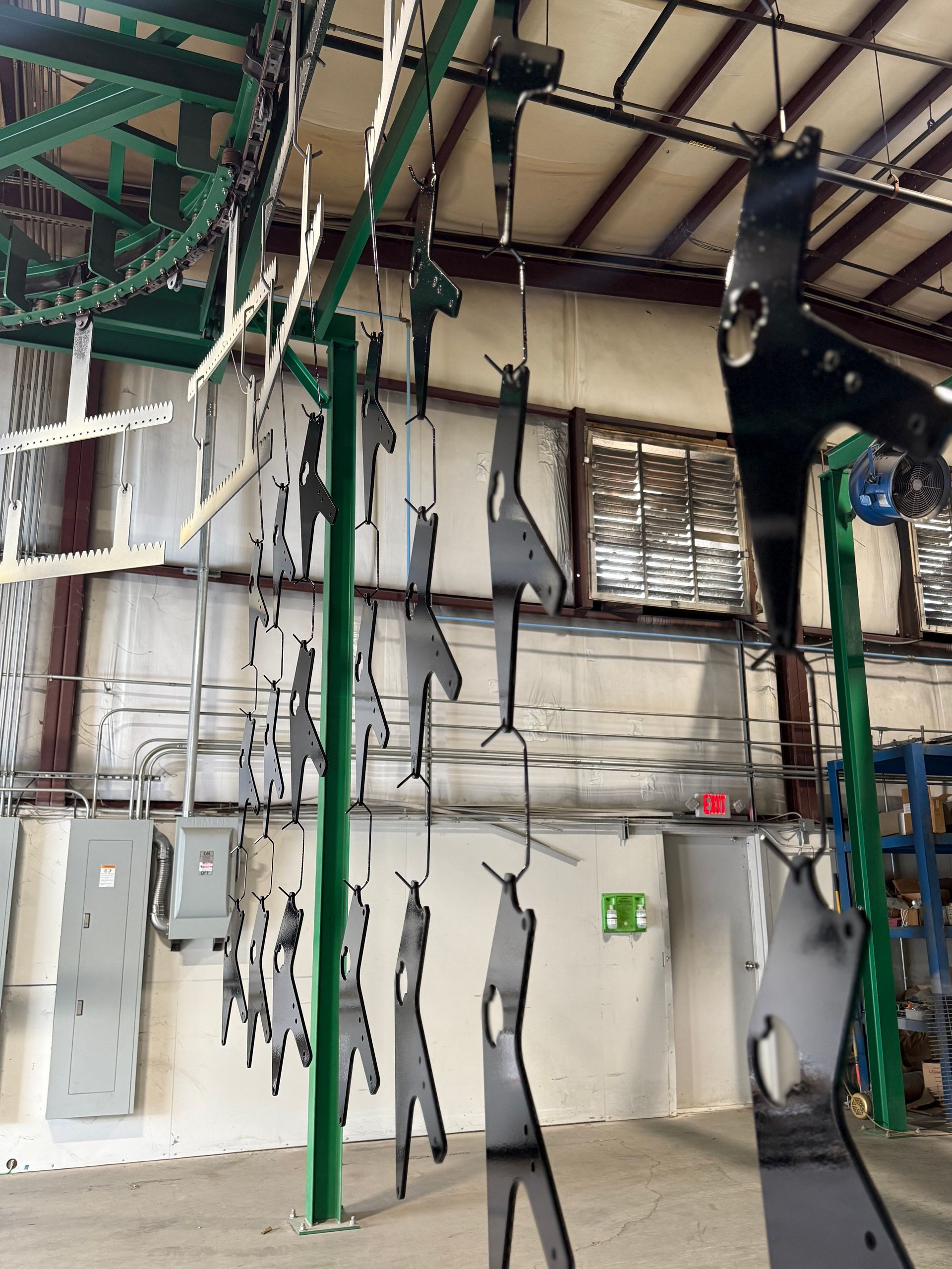 Indoor industrial space with hanging gray human-shaped figures and green support poles near a white wall.