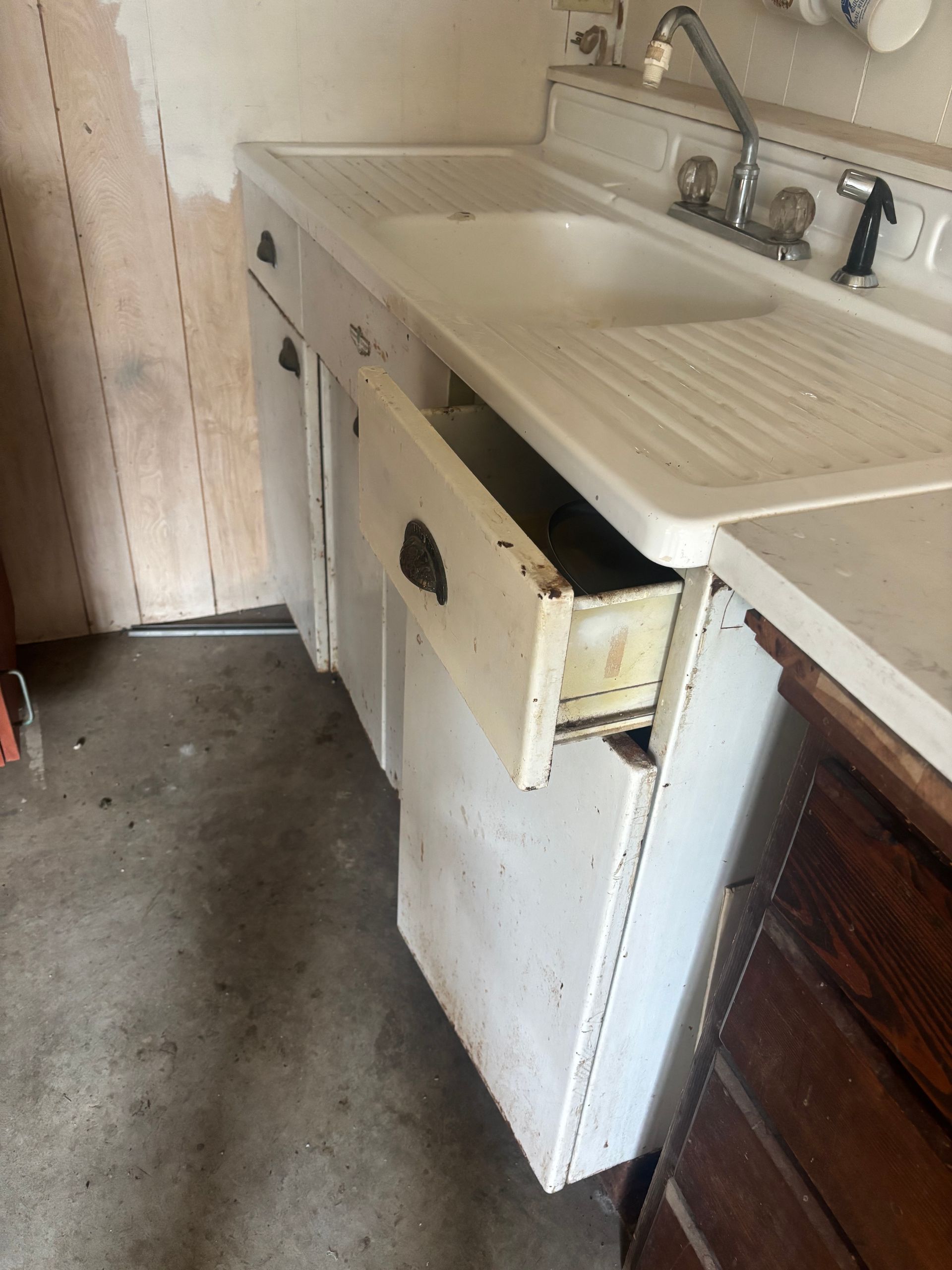 Damaged under-sink cabinet in a kitchen with a broken door and exposed interior.