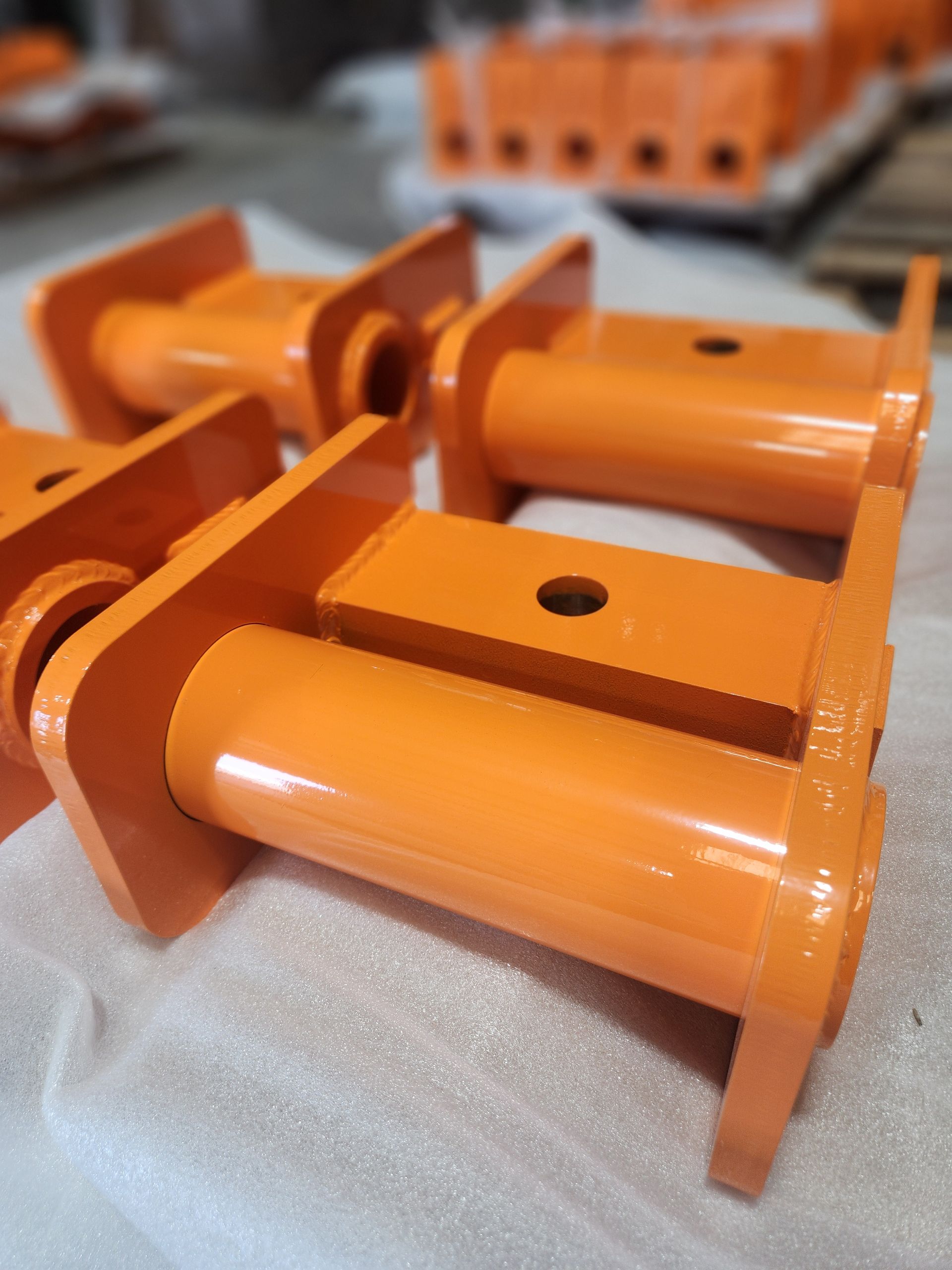 Orange metal industrial parts stacked on a padded surface, with more components blurred in the background