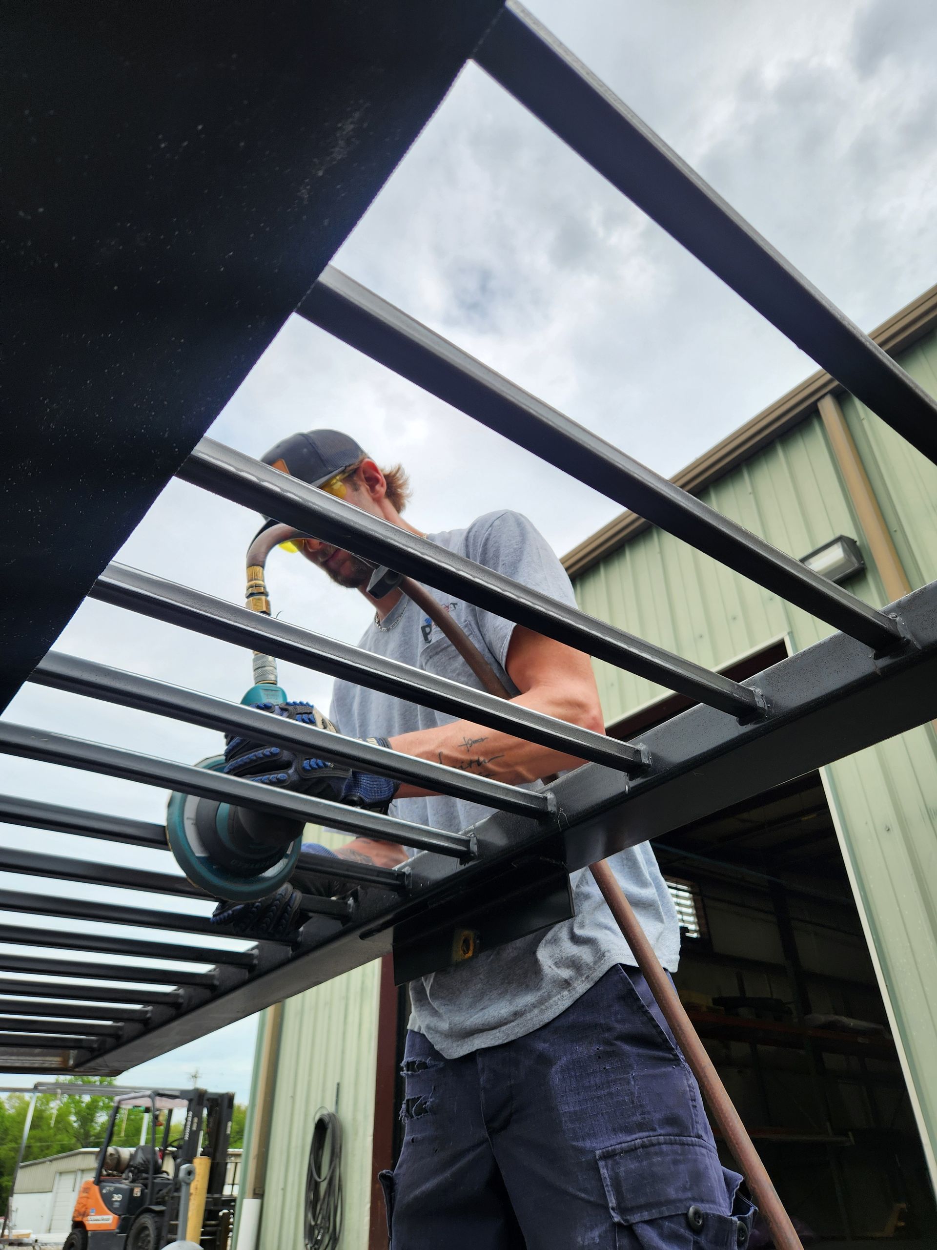 Worker installing a black metal frame beneath a light-colored roof outdoors