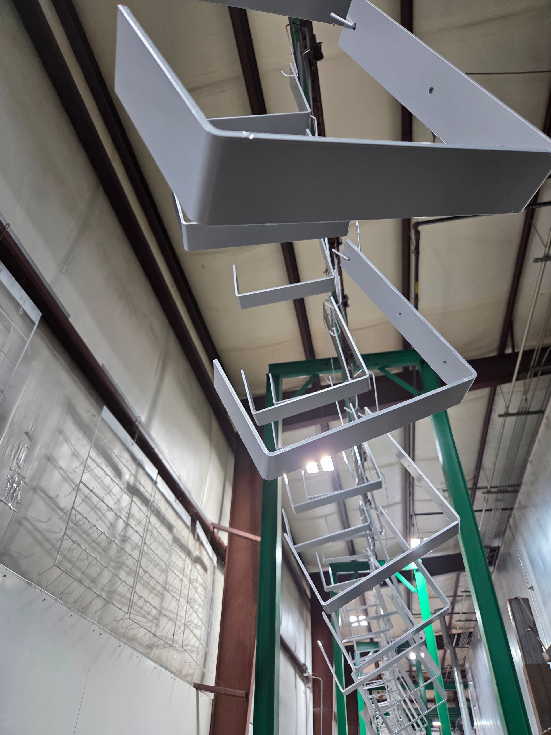 Suspended metal frames and ducts in an industrial warehouse ceiling with green support beams and skylights