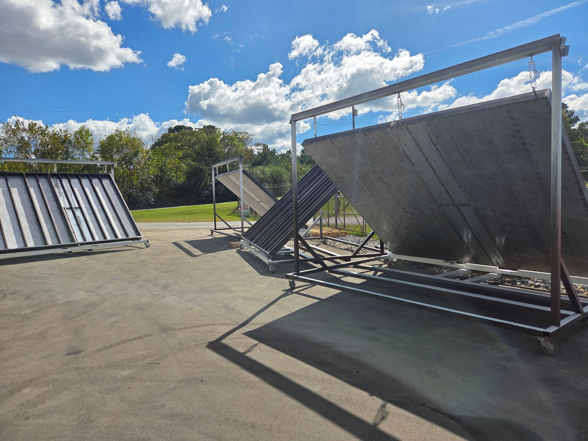 Outdoor solar panel mounting frames in a sunny open lot with blue sky and clouds.