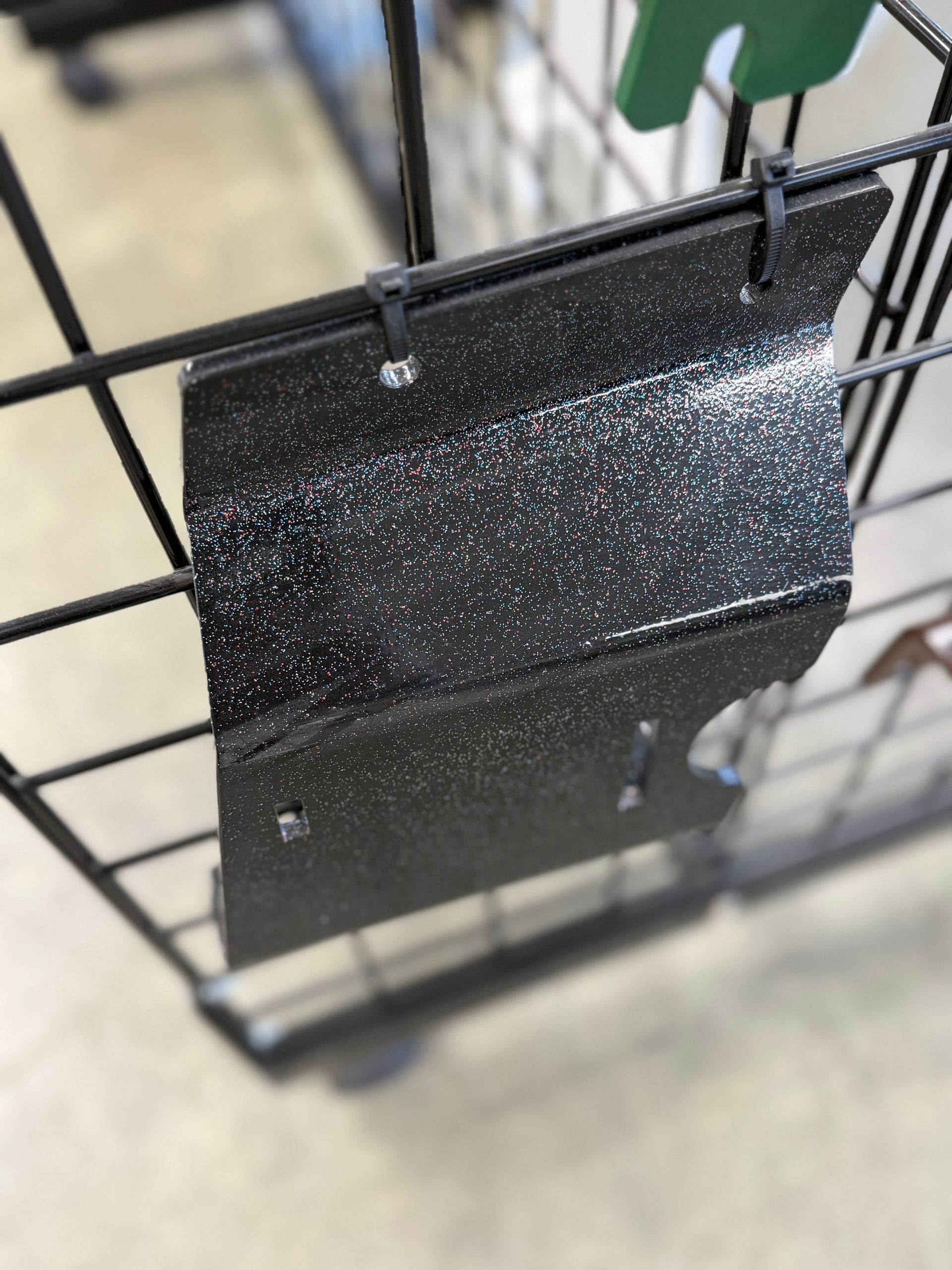 Black speckled metal sign attached to a wire grid rack in a store aisle