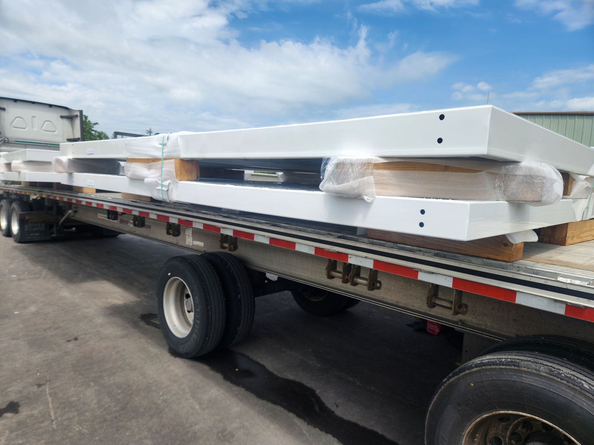 Flatbed truck carrying wrapped white construction beams on a roadside under a blue sky
