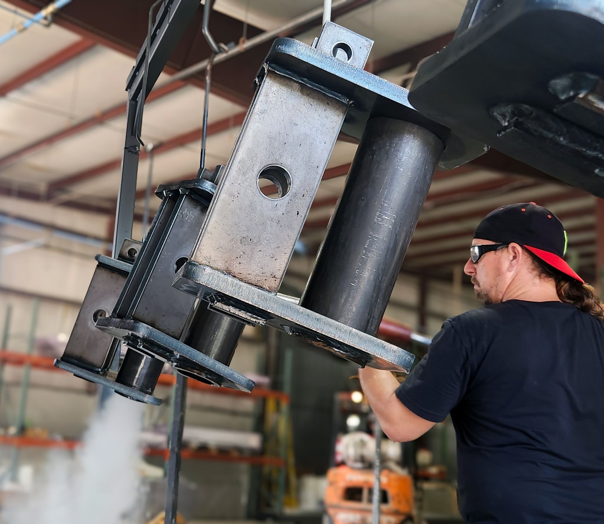 Worker in a warehouse installing a large black metal machine on a ceiling mount.