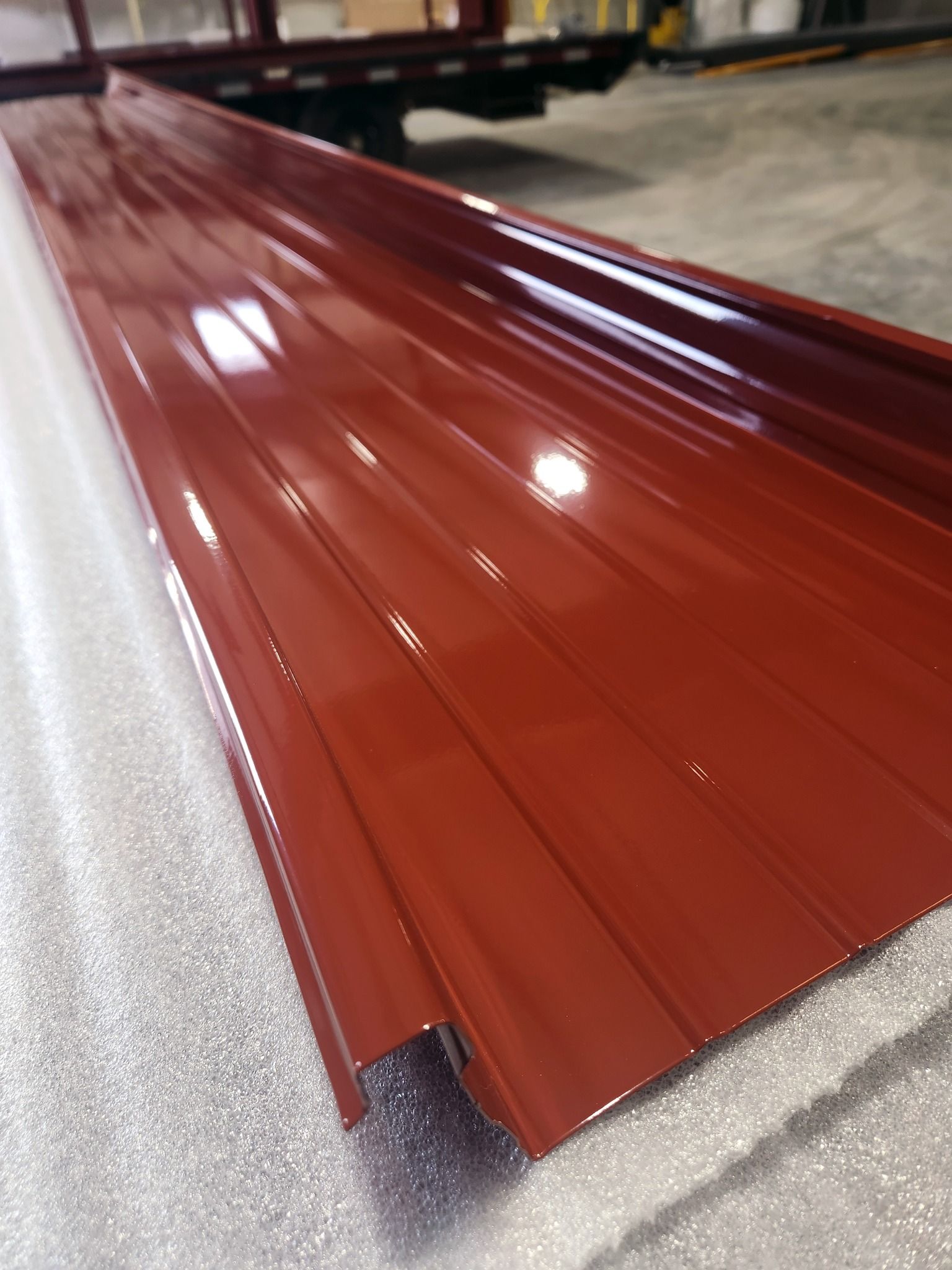 Glossy red corrugated metal roofing panel on a foam surface in a workshop