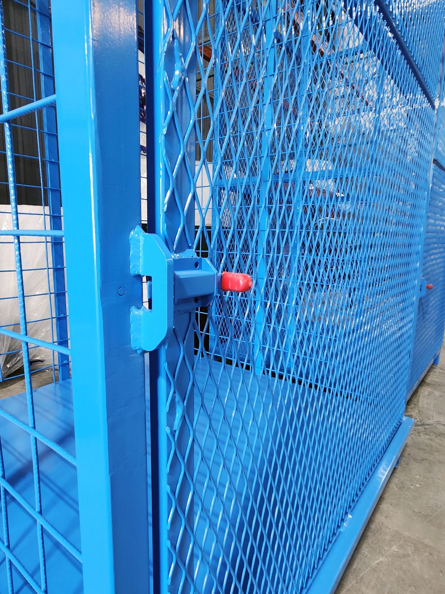 Blue metal mesh gate with a red latch beside a concrete walkway