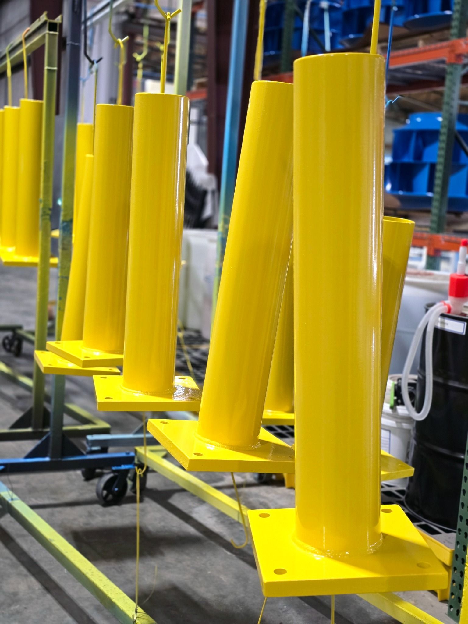 Yellow industrial parts hanging in a factory, with rows of metal frames and equipment in the background.
