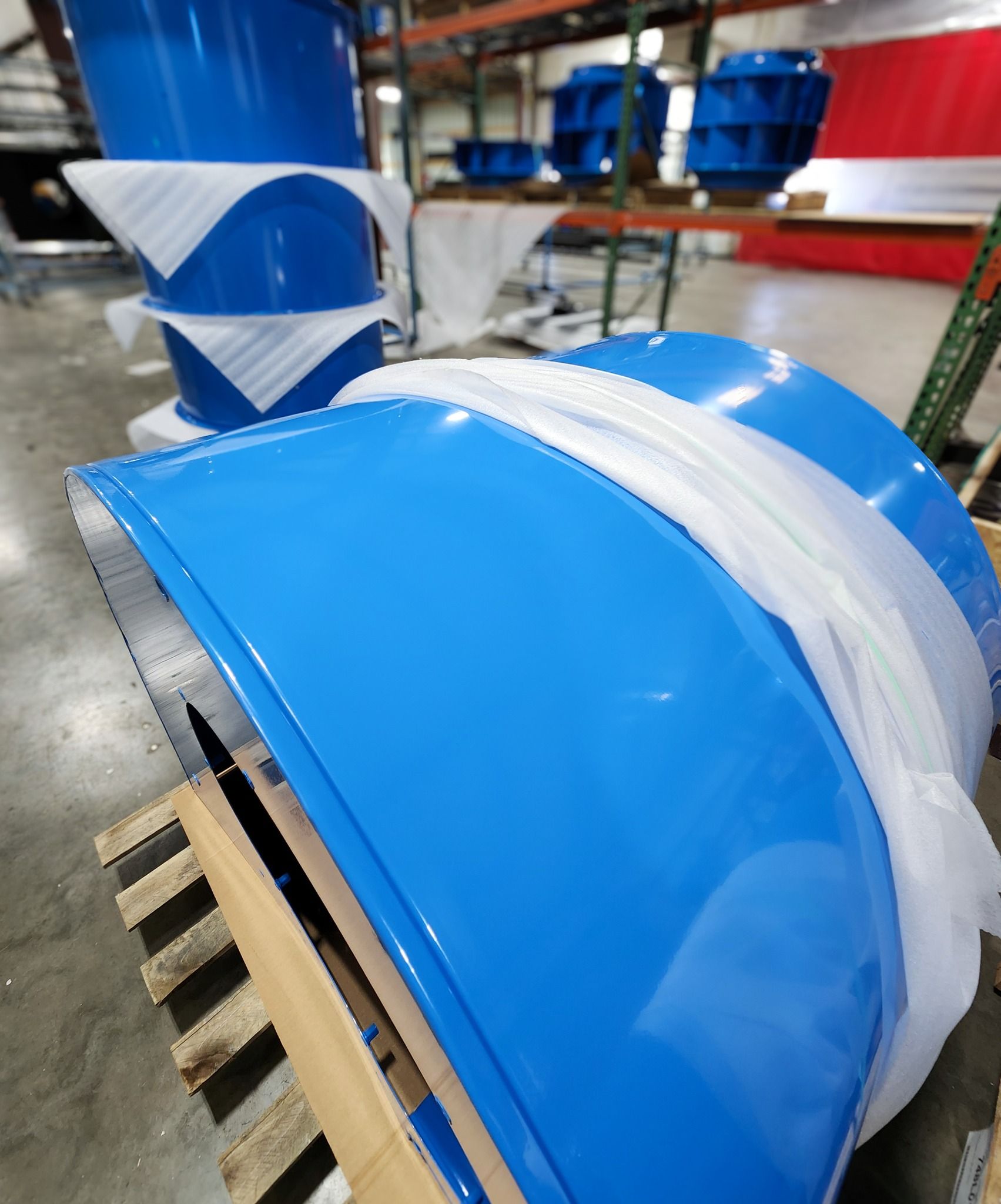Blue industrial ducts or tanks wrapped in white plastic bands in a warehouse setting