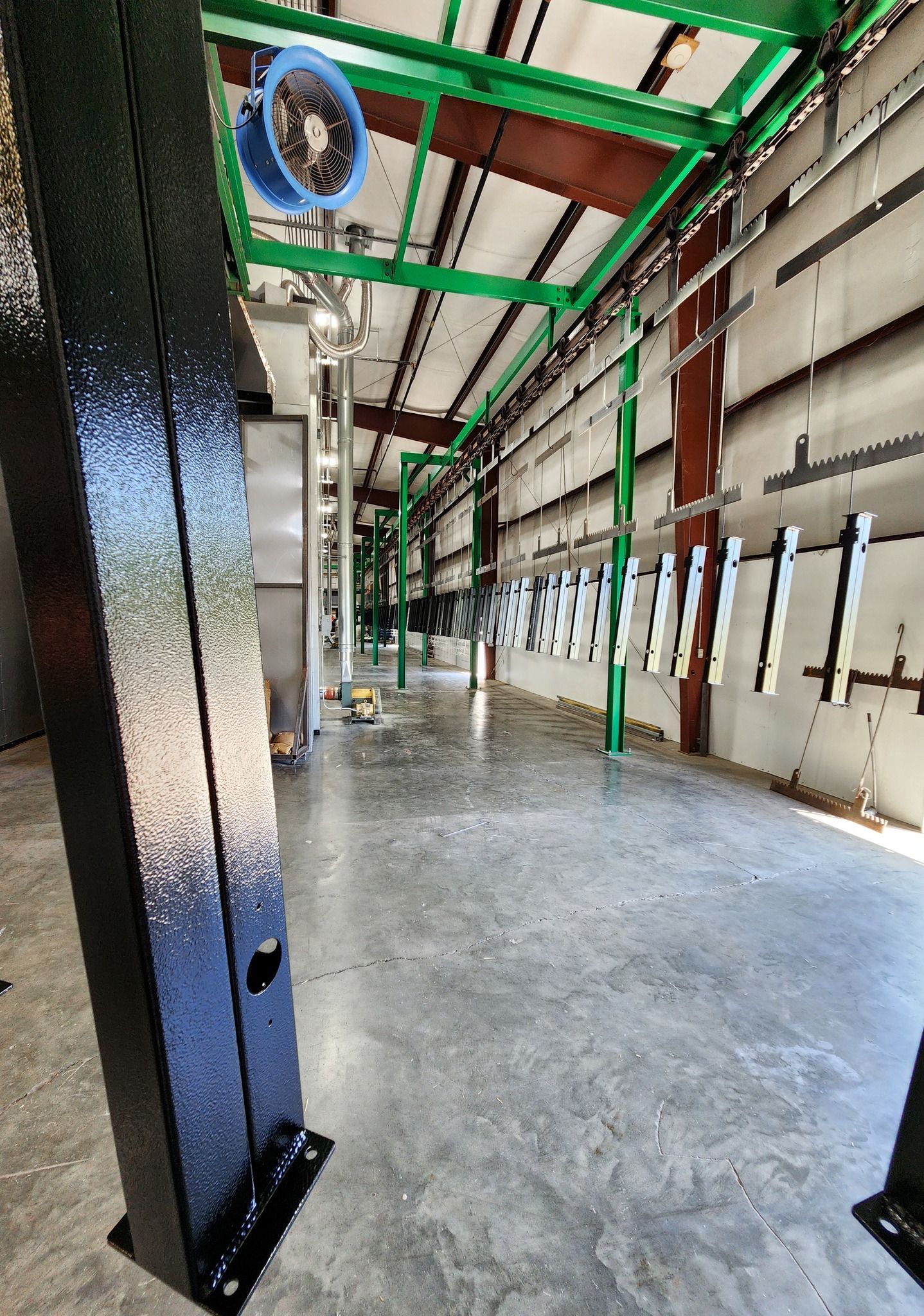 Industrial warehouse interior with concrete floor, green steel beams, and a black column in the foreground