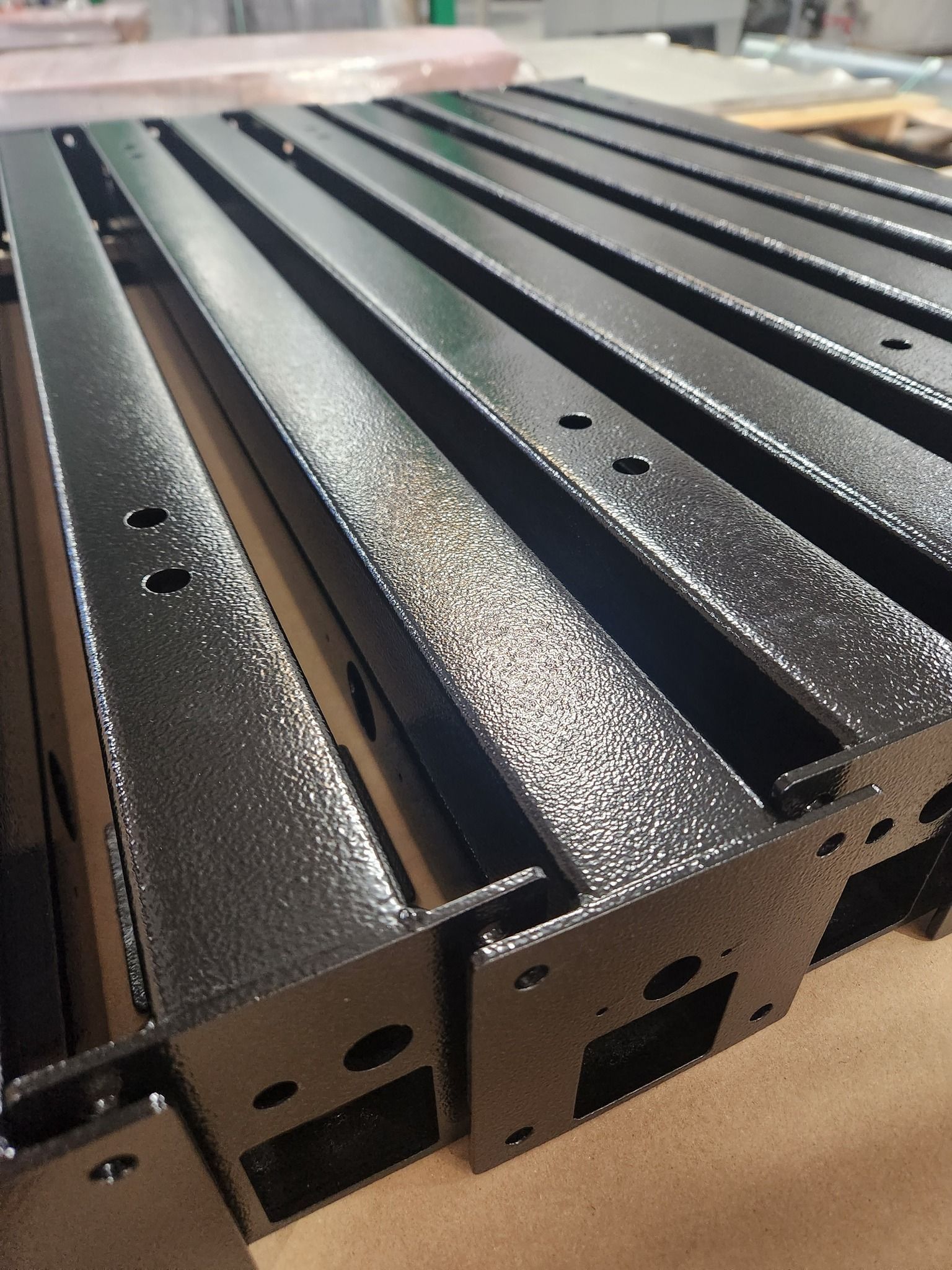 Black perforated metal rails lined up on a cardboard surface in close-up.