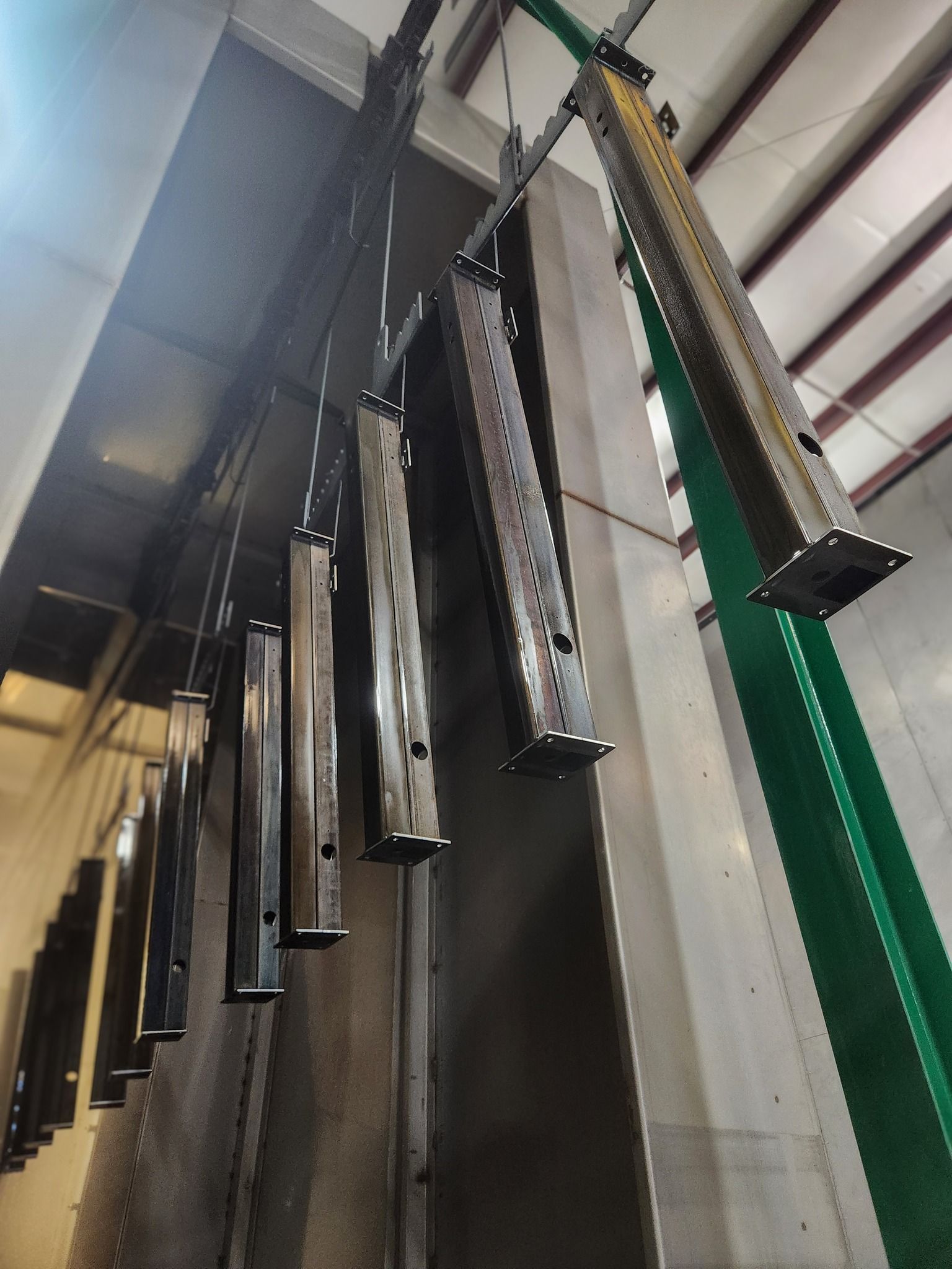 Row of hanging metal tools or parts beside a green rack in an industrial workspace