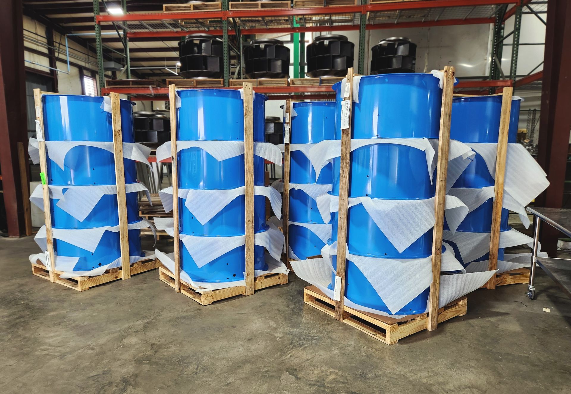 Blue industrial barrels wrapped in white packaging on wooden pallets in a warehouse