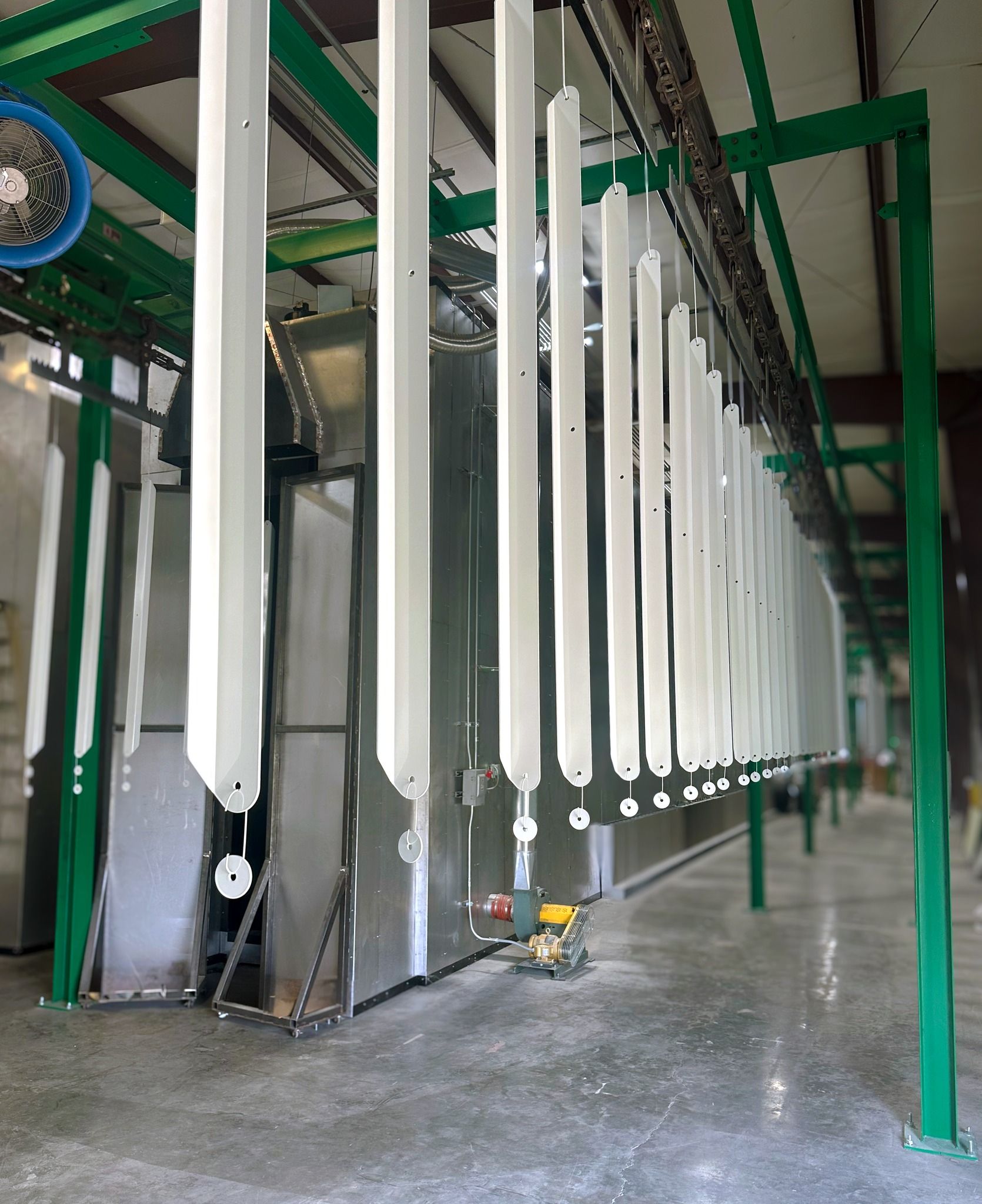 Industrial paint line with rows of white hanging parts in a green metal frame workshop