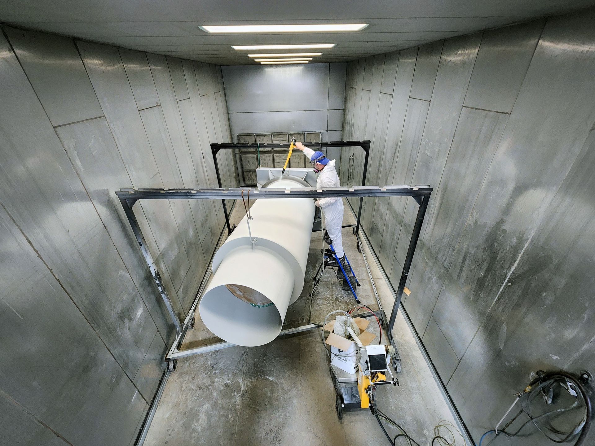 Workers in a tunnel-like chamber guiding a large white pipe into place with tools and equipment