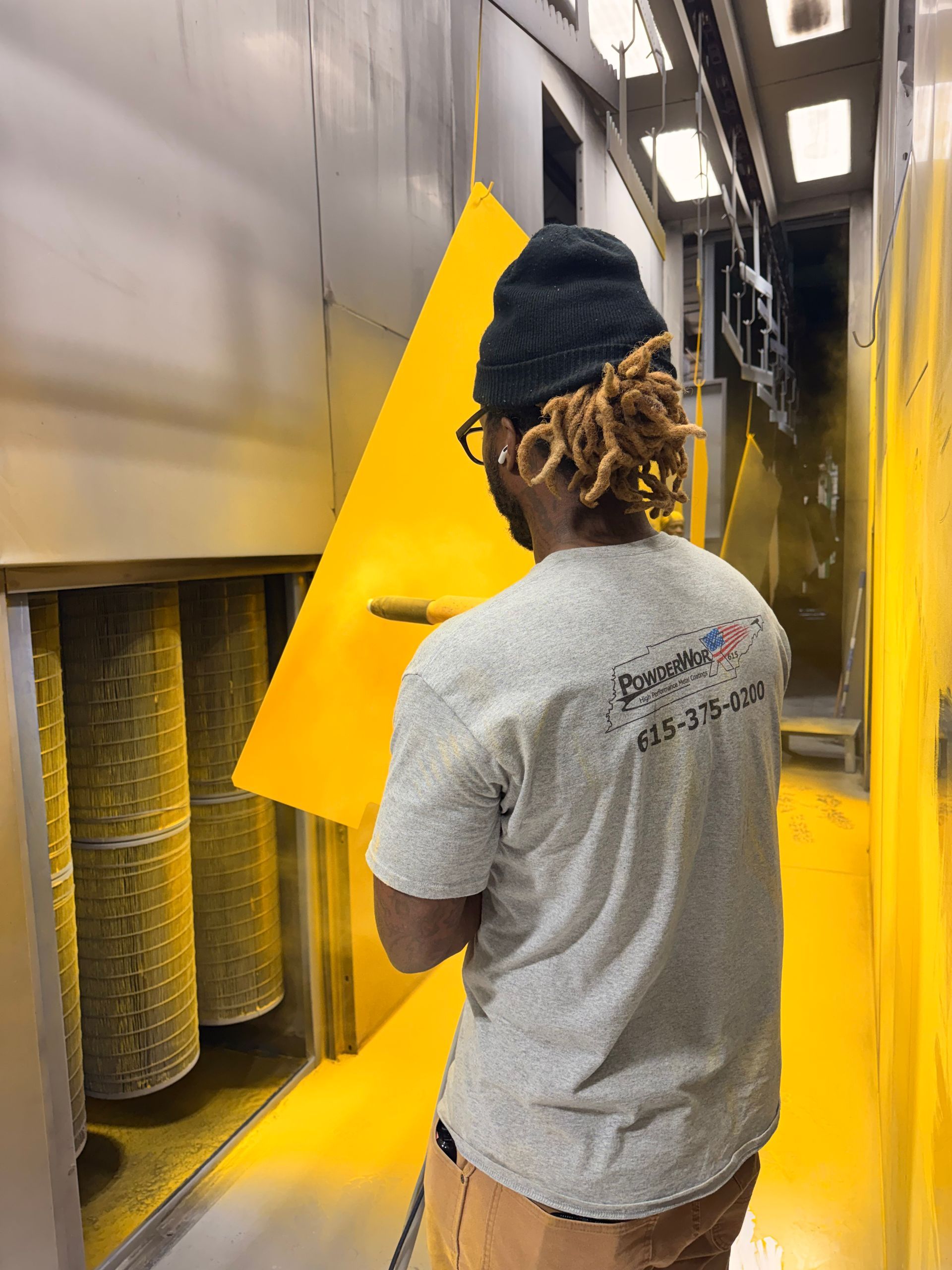 Worker in gray shirt and black beanie opening a large yellow industrial machine panel.