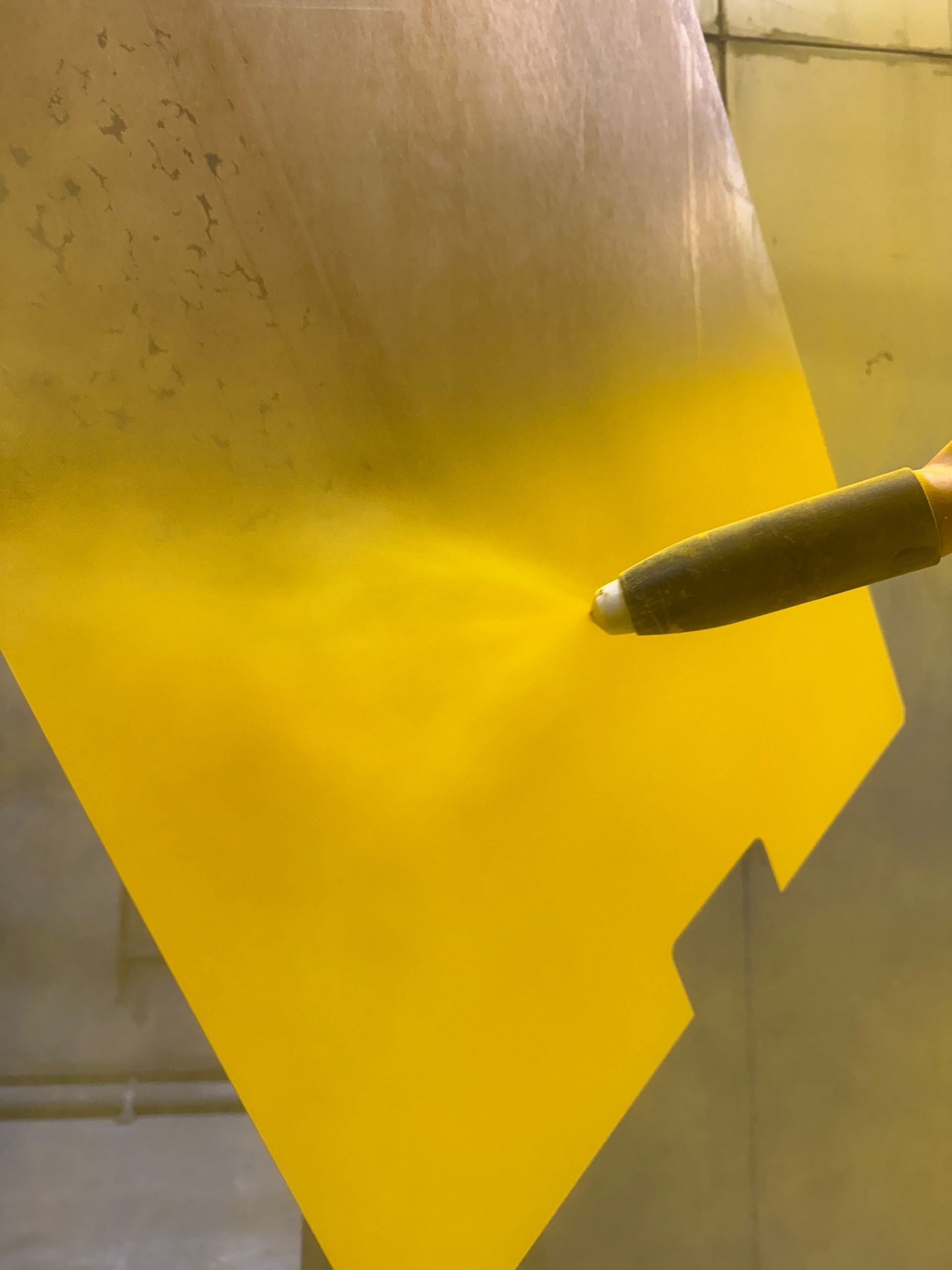 Yellow paint spraying onto a metal surface from a nozzle.