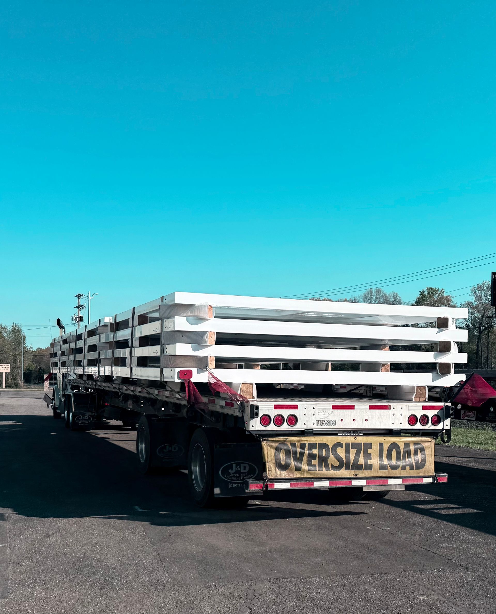 Flatbed truck carrying stacked white plastic chairs on a sunny street, with a “SERVICE LOAD” sign at the rear
