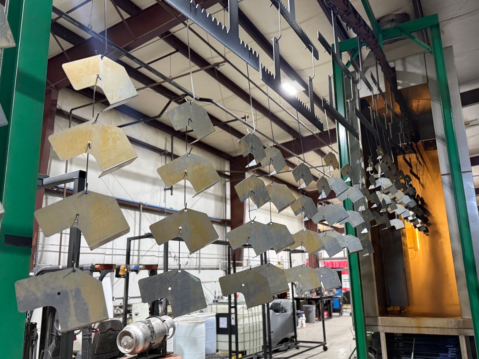 Industrial workshop with rows of suspended metal parts and machinery under a high ceiling