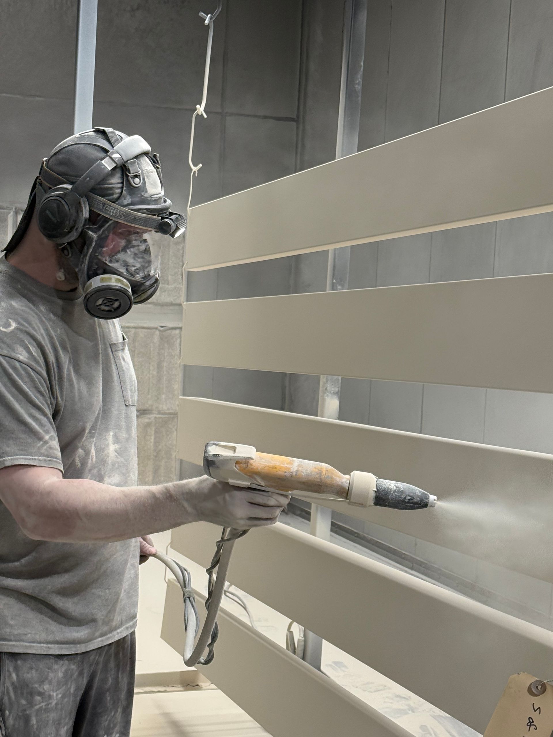 Person spray-painting a slatted fence while wearing a respirator and gloves.