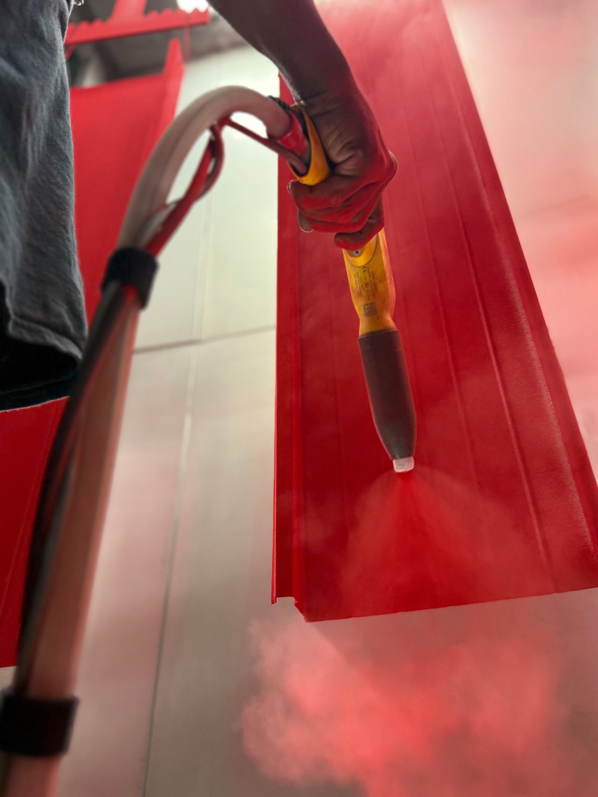 Person spray-painting a red surface with a spray gun, creating red mist