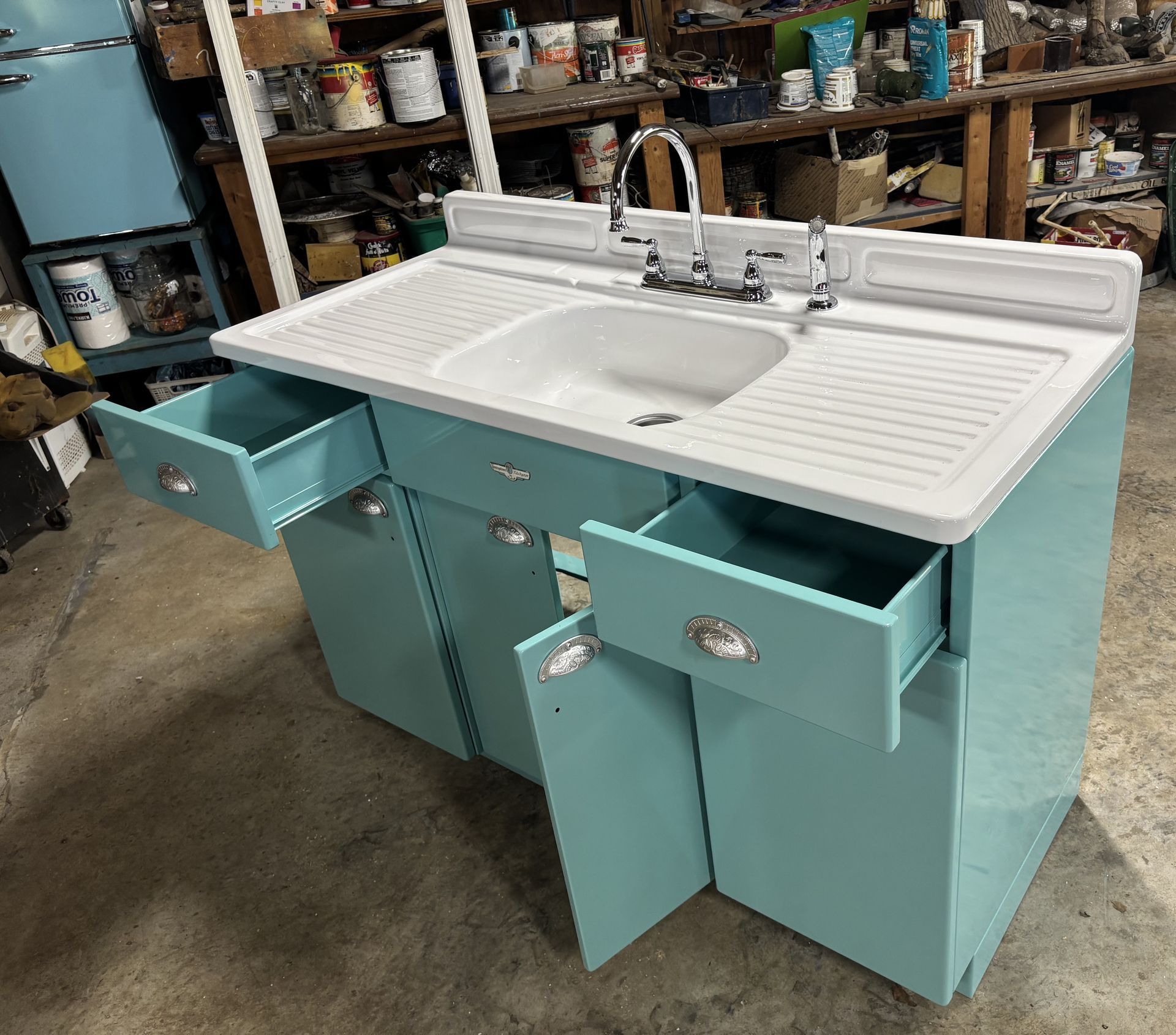Turquoise double-sink bathroom vanity with white countertop and open cabinets in a workshop
