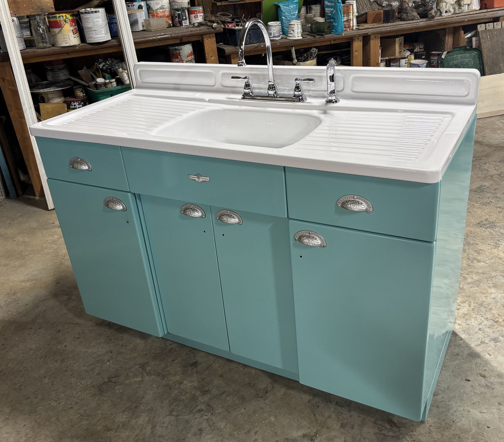 Turquoise bathroom vanity with white sink and chrome faucet in a workshop setting