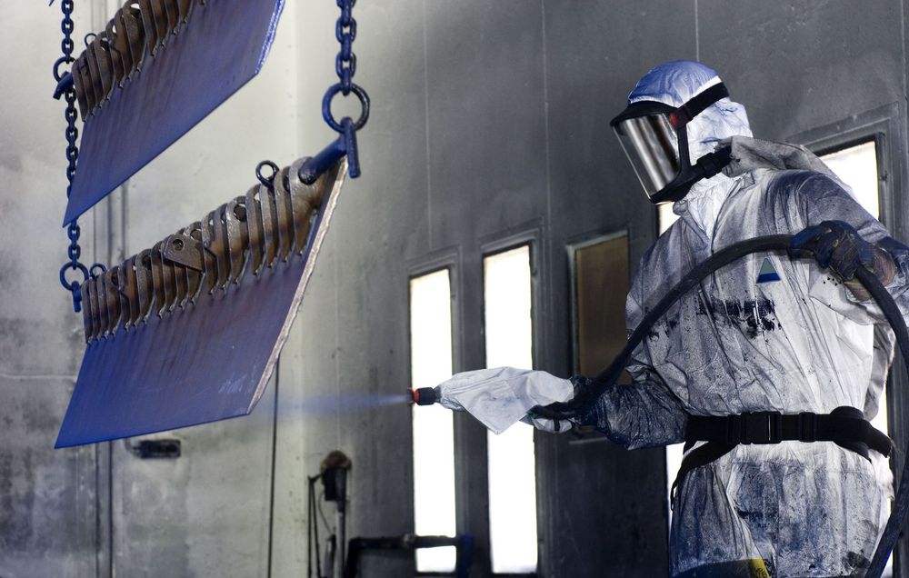 Person in protective gear spray-painting metal blades in a spray booth.