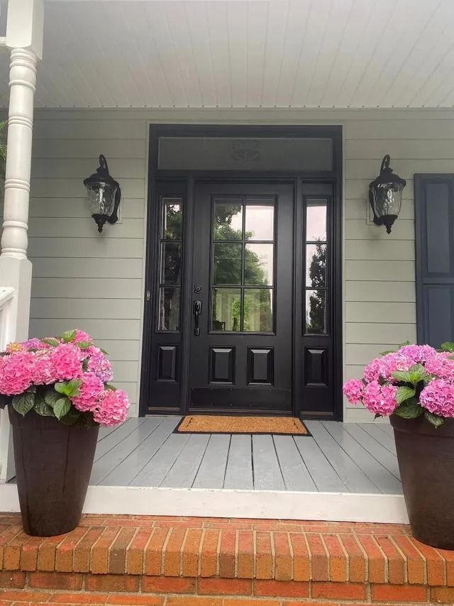 A black door with pink flowers in front of it on a porch.
