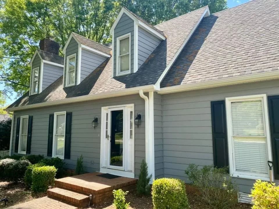 A gray house with black shutters and a brown roof