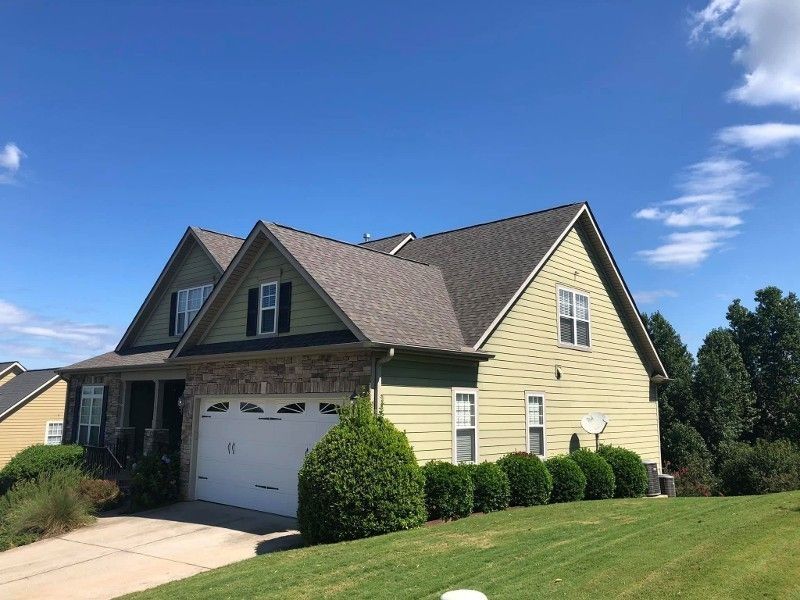 A green house with a white garage door is sitting on top of a lush green hillside.