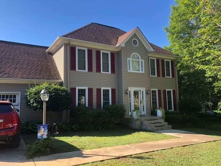 A large house with red shutters and a red suv parked in front of it.