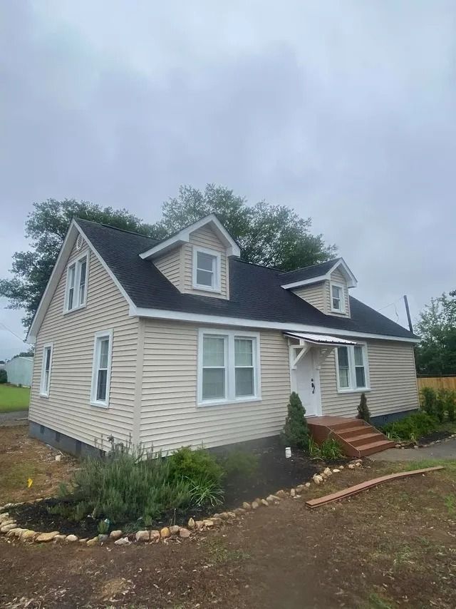 A house with a black roof and white siding is sitting on top of a dirt field.