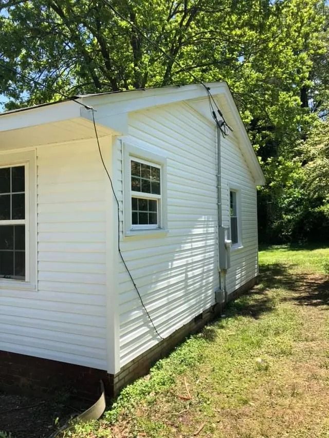 The side of a white house with a window and a drain pipe.