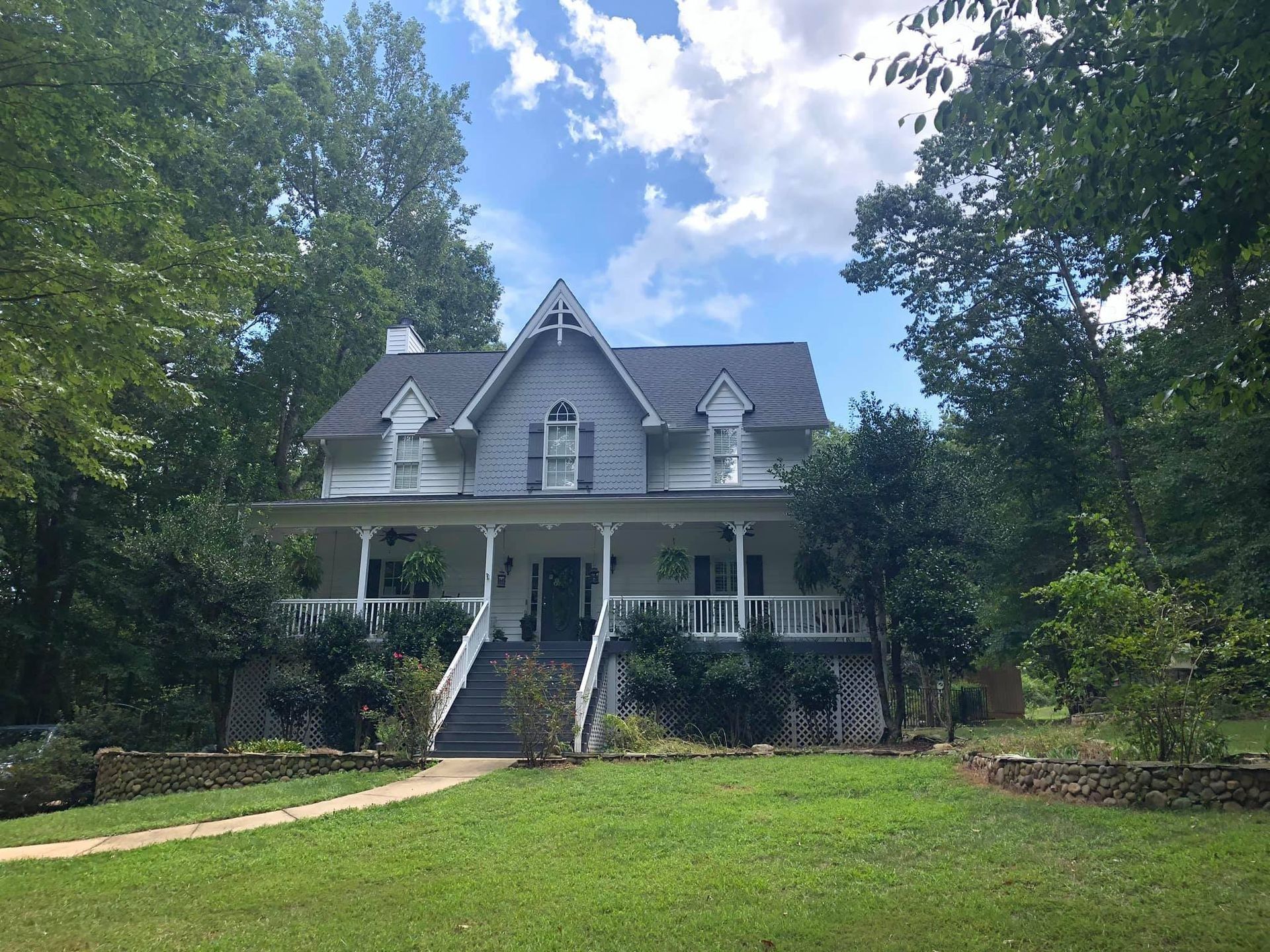 A large white house with a large porch is surrounded by trees.