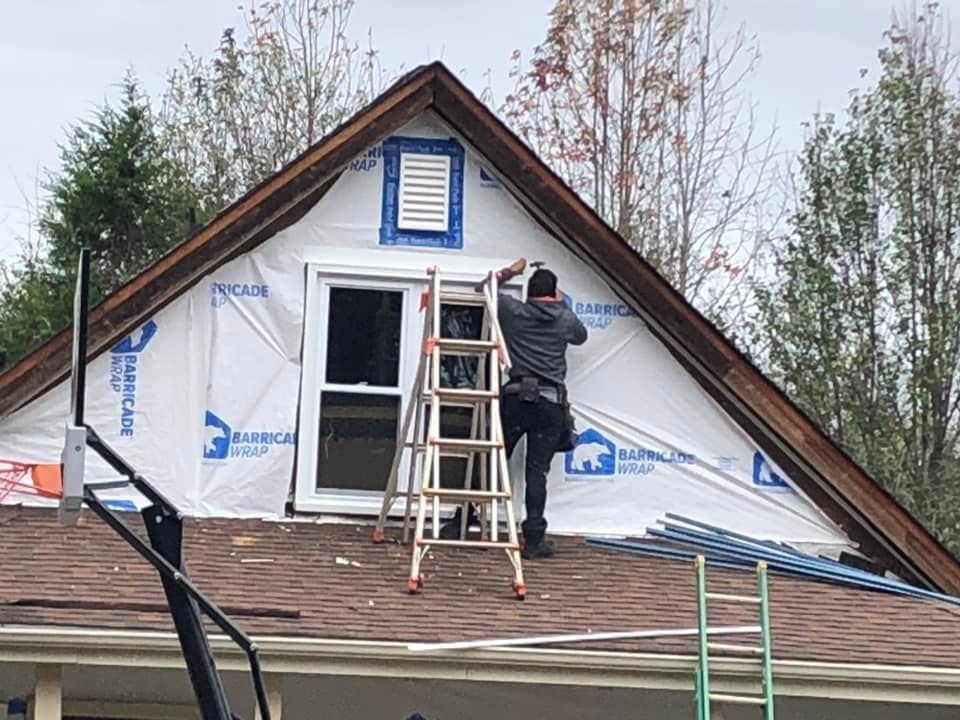 A man is standing on a ladder on the roof of a house.