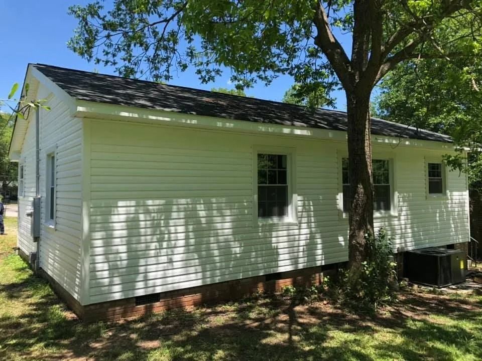 A white house with a black roof and a tree in front of it.