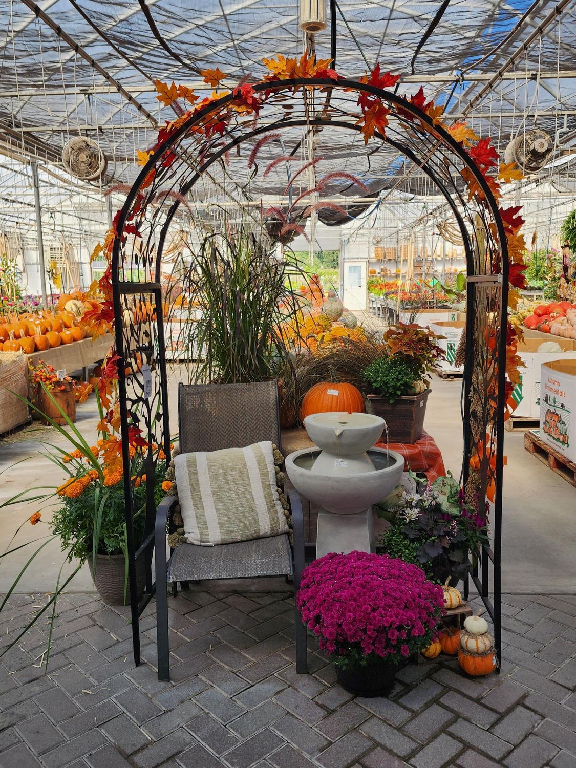 Decorative autumn garden arch with flowers, potted plants, and a bench on a paved patio
