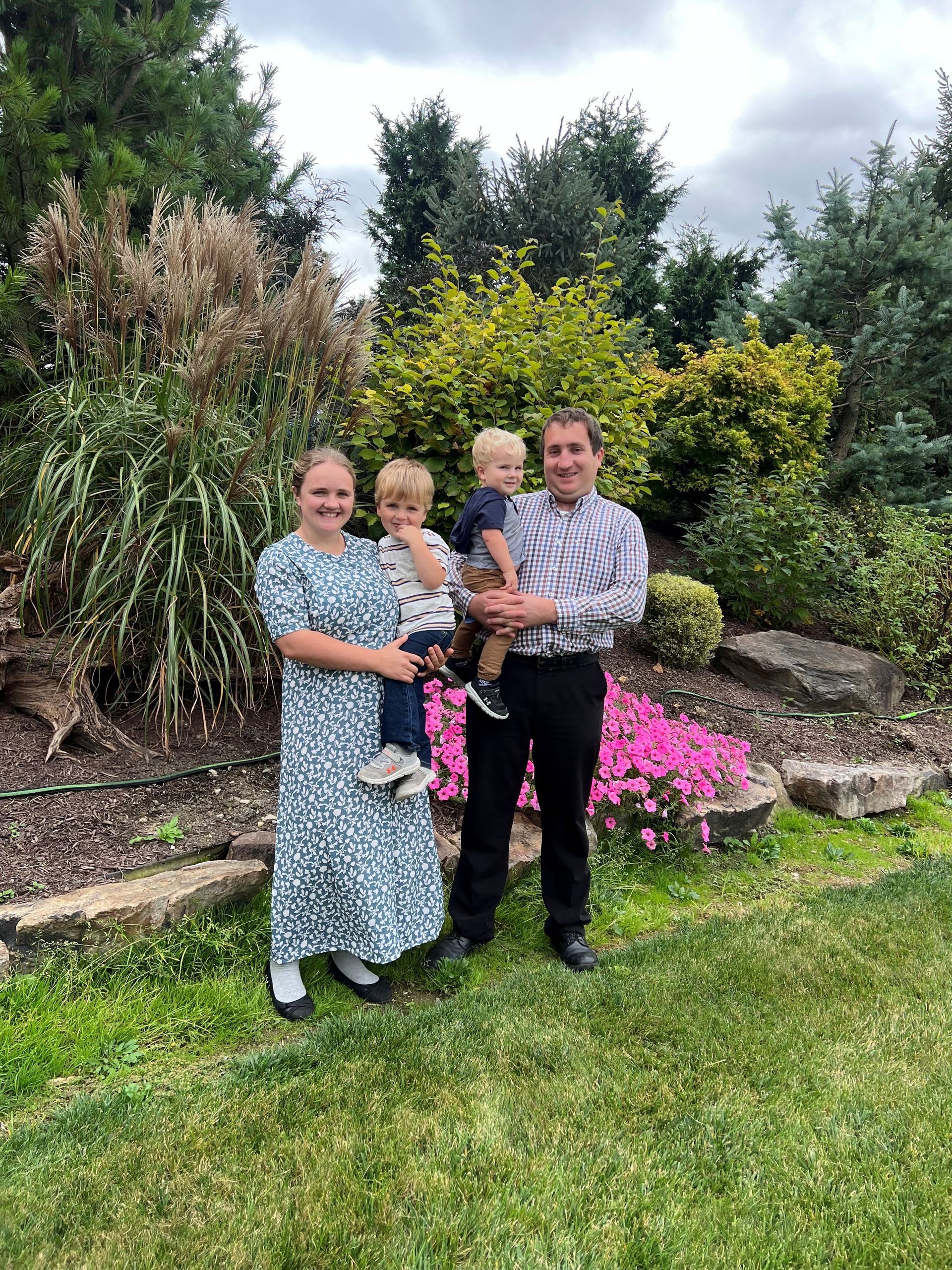 Family of four poses outdoors in front of a garden.