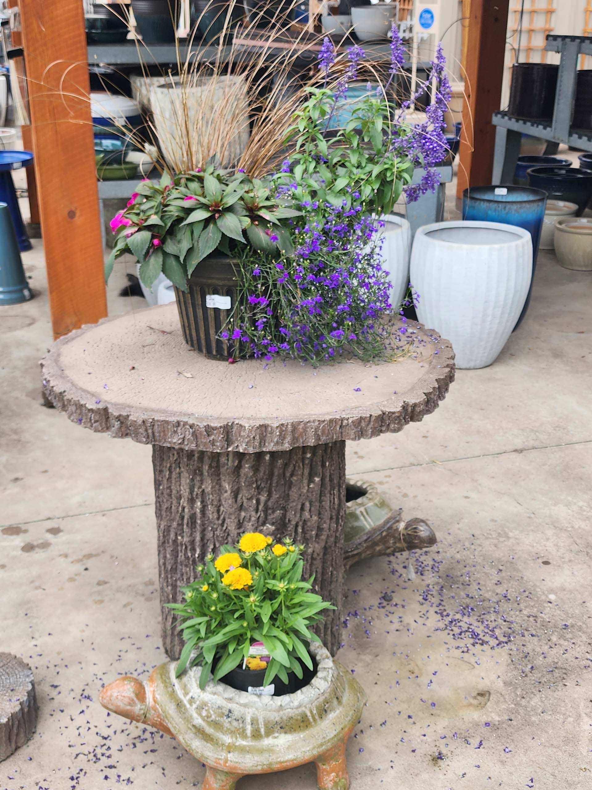 Potted flowers on a rustic tree-stump table with a smaller flower pot in front
