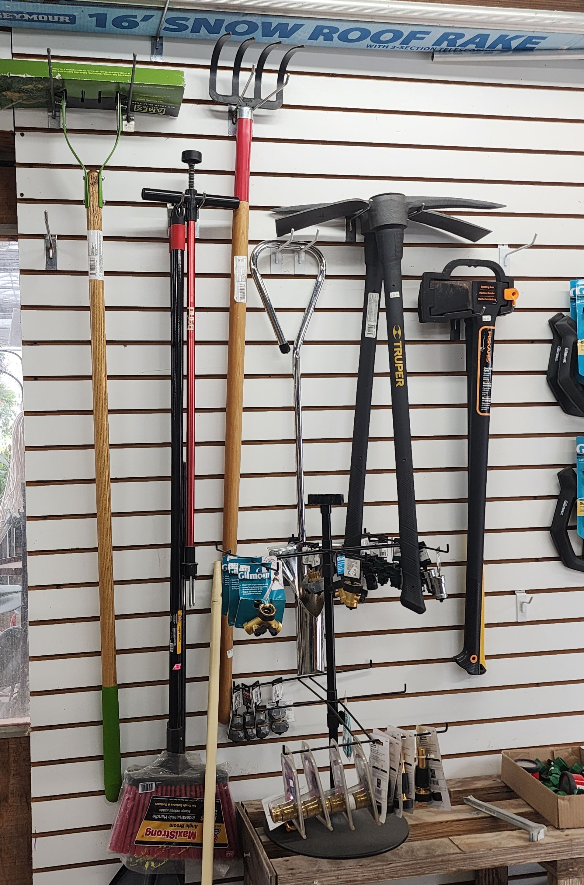 Snow-removal tools hanging on a shop wall, including shovels, rakes, and a snow blower handle.