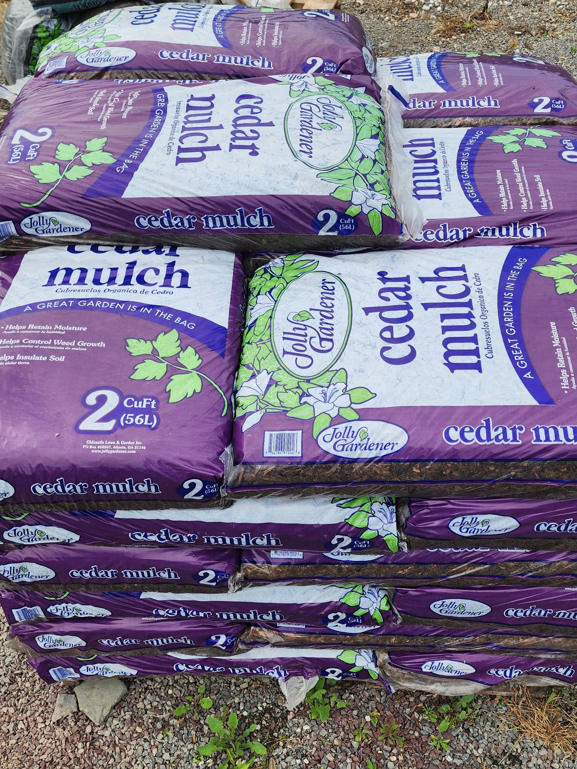Stacked purple bags of cedar mulch outdoors on gravel.
