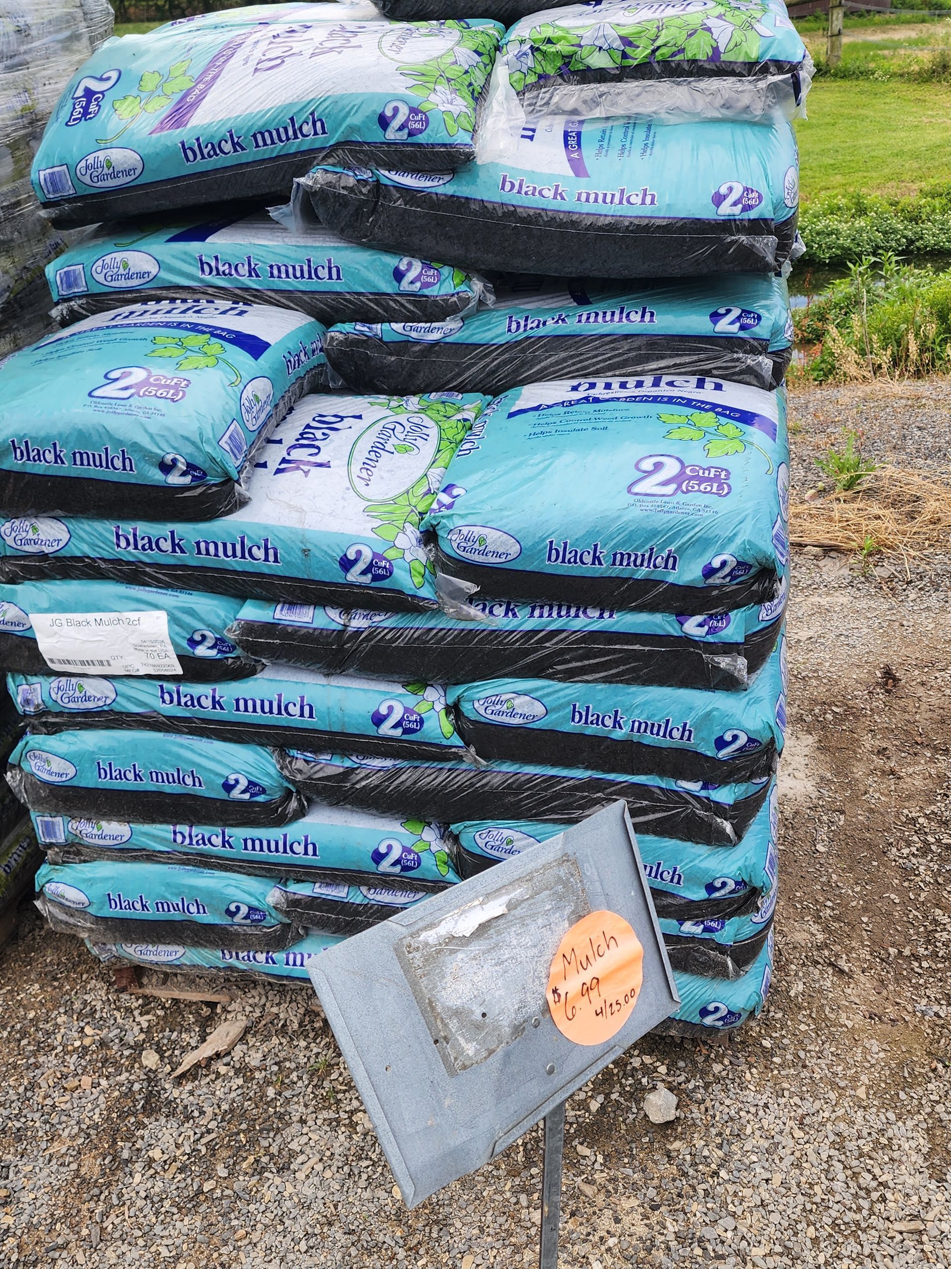 Stacked bags of garden soil with a small metal shovel on gravel outdoors