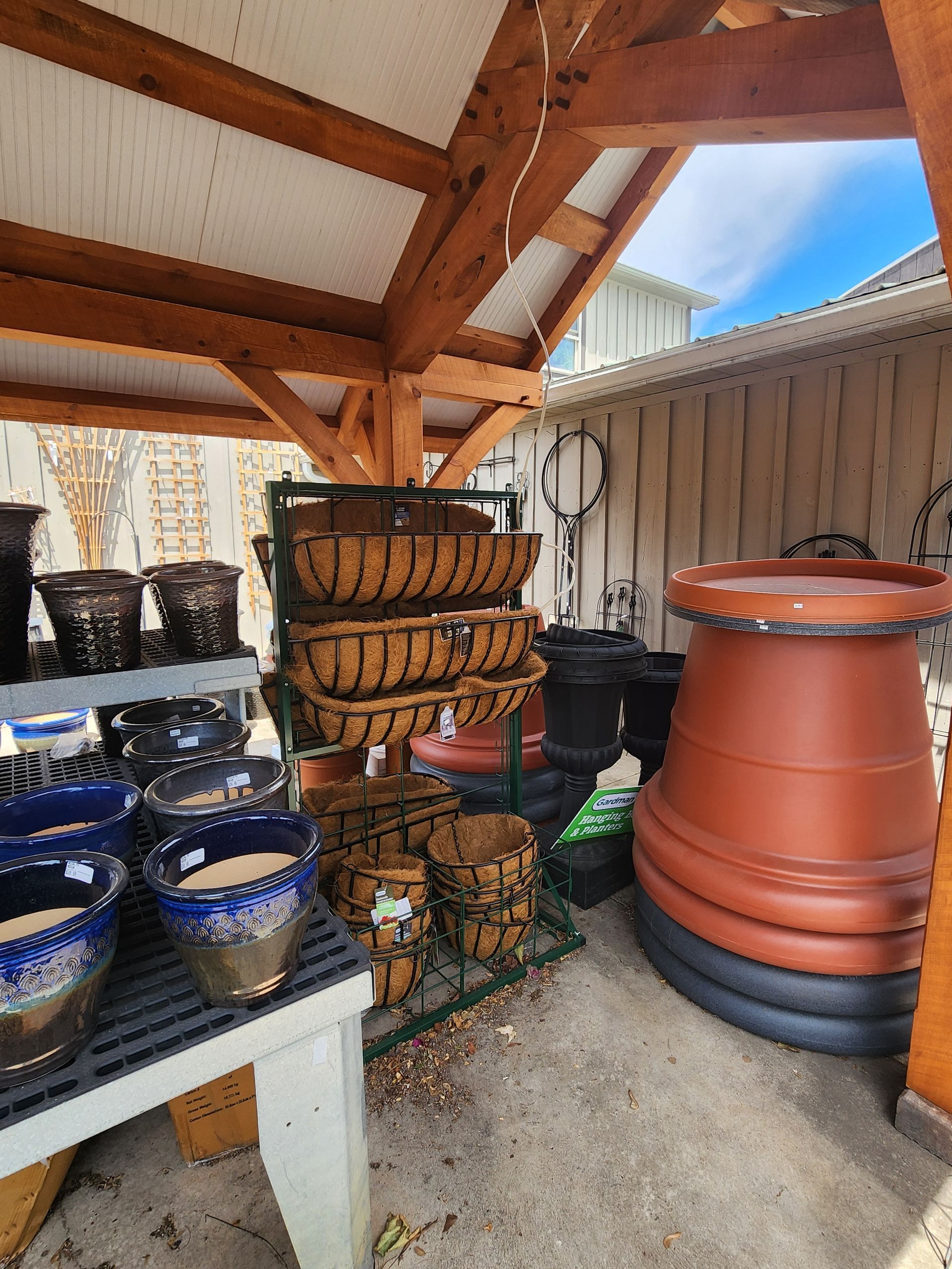 Covered outdoor storage area with stacked plant pots, baskets, and garden supplies