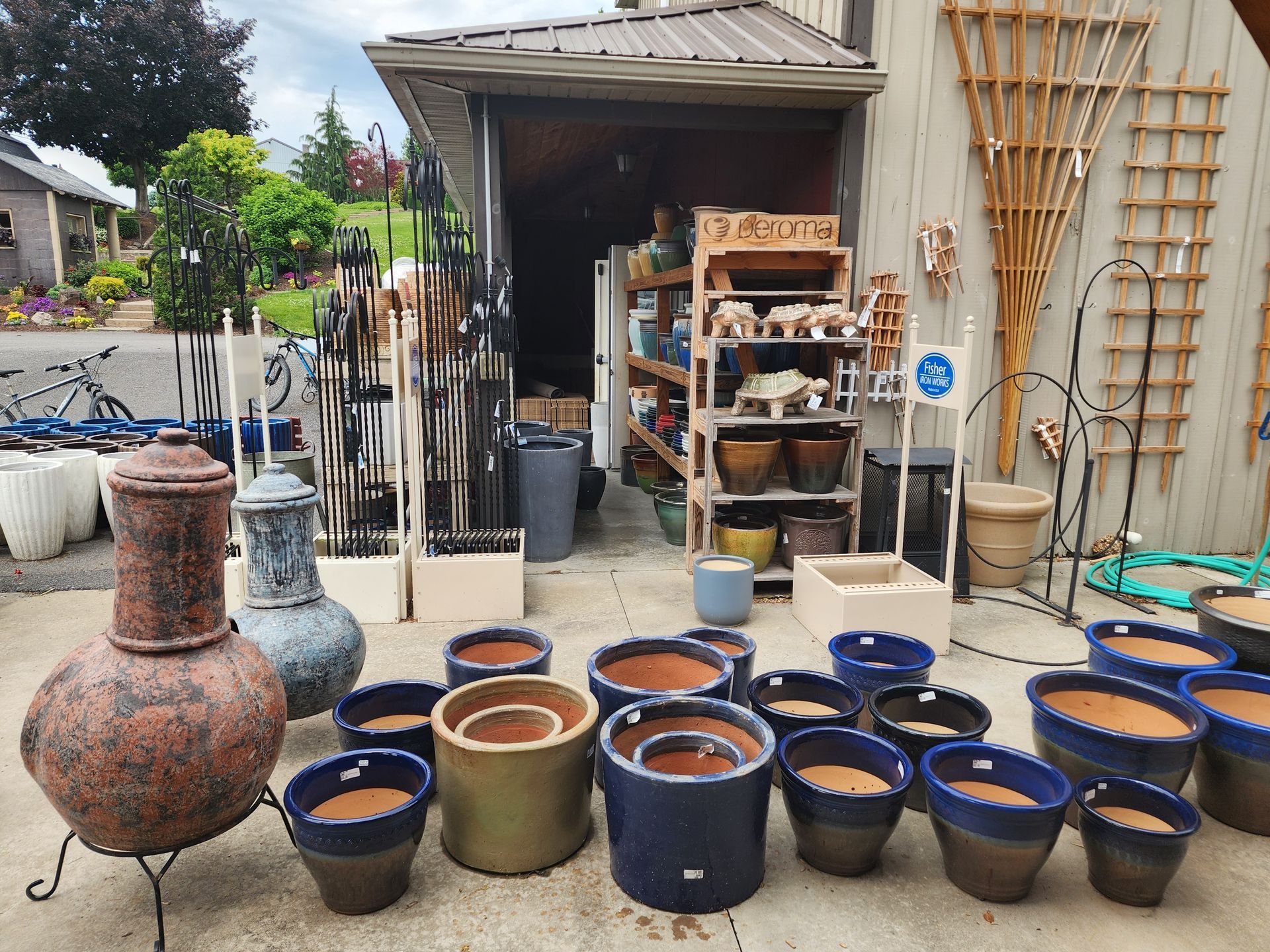 Outdoor pottery display with blue, brown, and tan glazed pots arranged outside a workshop.